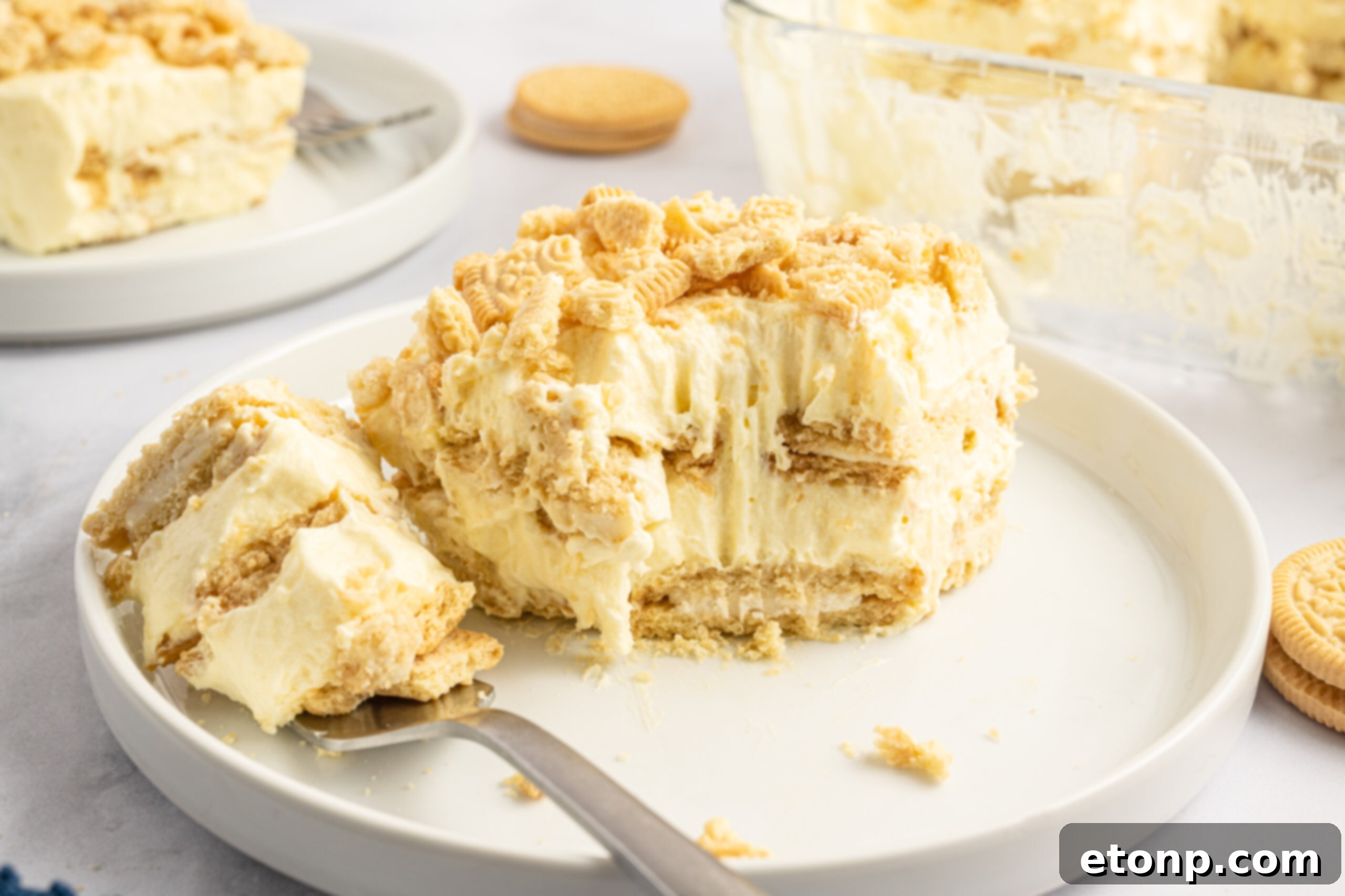 Front view of a slice of Golden Oreo Icebox Cake on a white plate with a bite removed by a silver fork, inviting to taste.