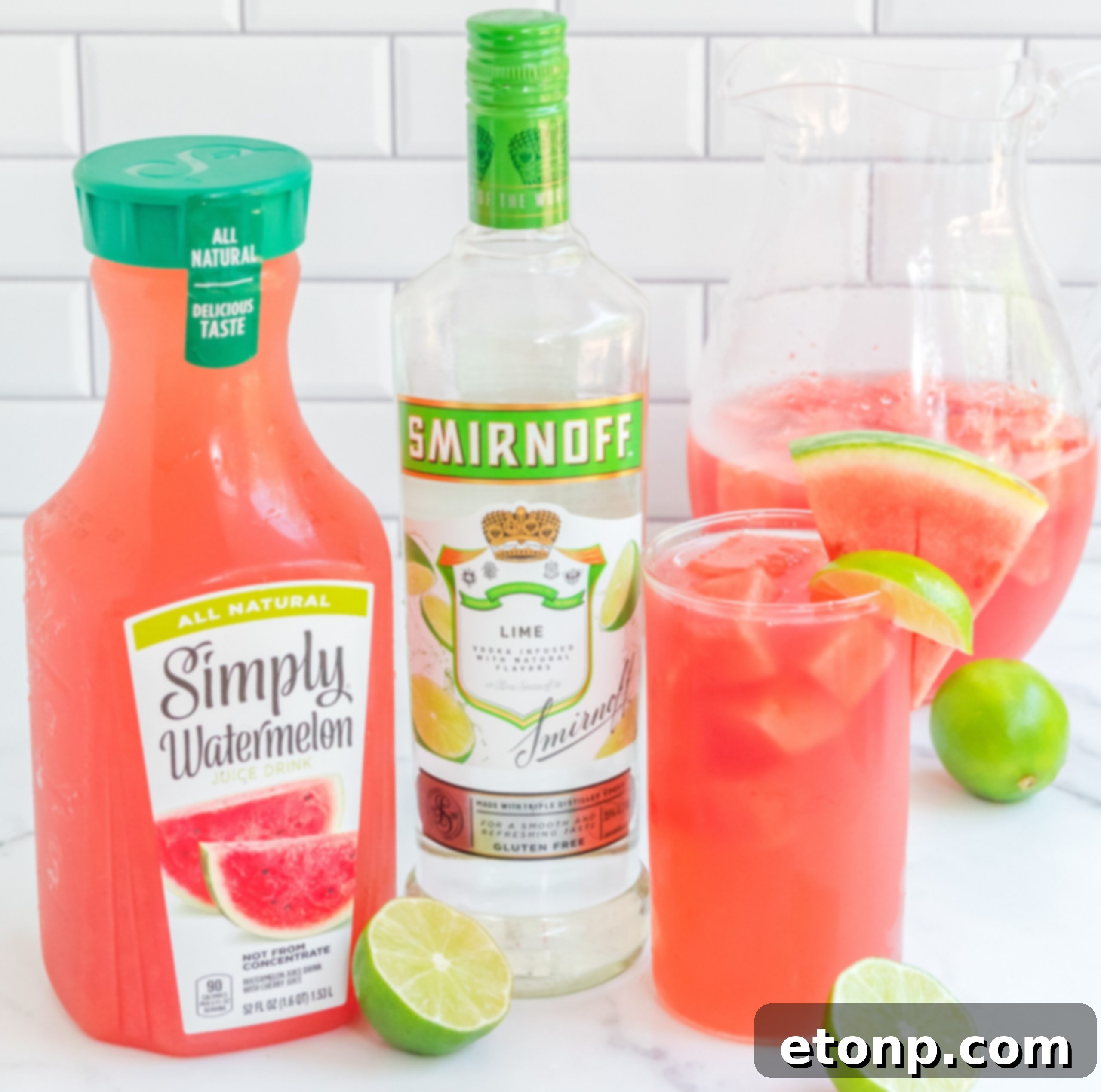 Front view of Watermelon Cocktail in a clear glasses garnished with lime and watermelon slices next wo watermelon juice bottle and a vodka bottle