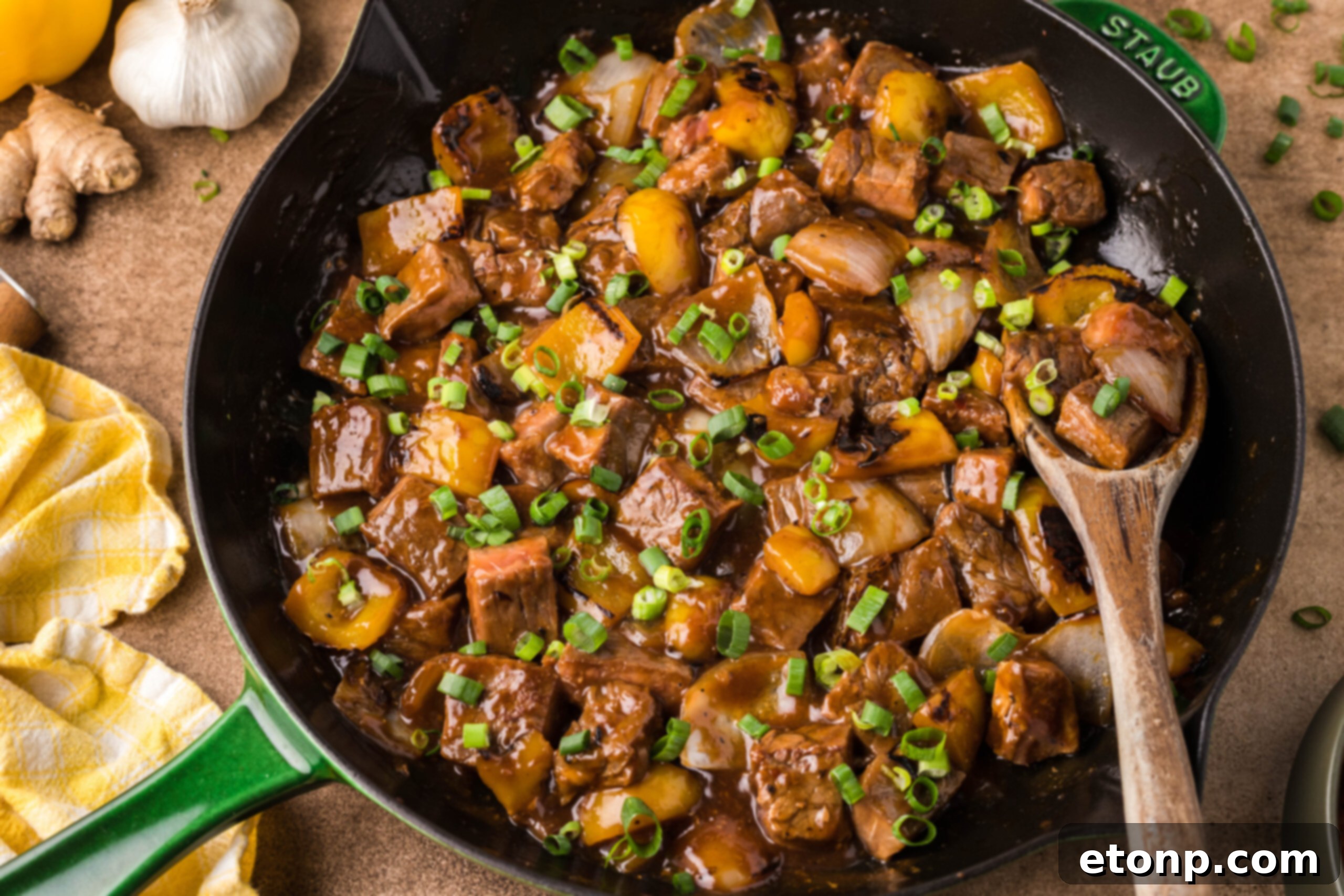 Front view of Teriyaki Steak Bites in a black and green skillet with a wooden spoon in the pan,