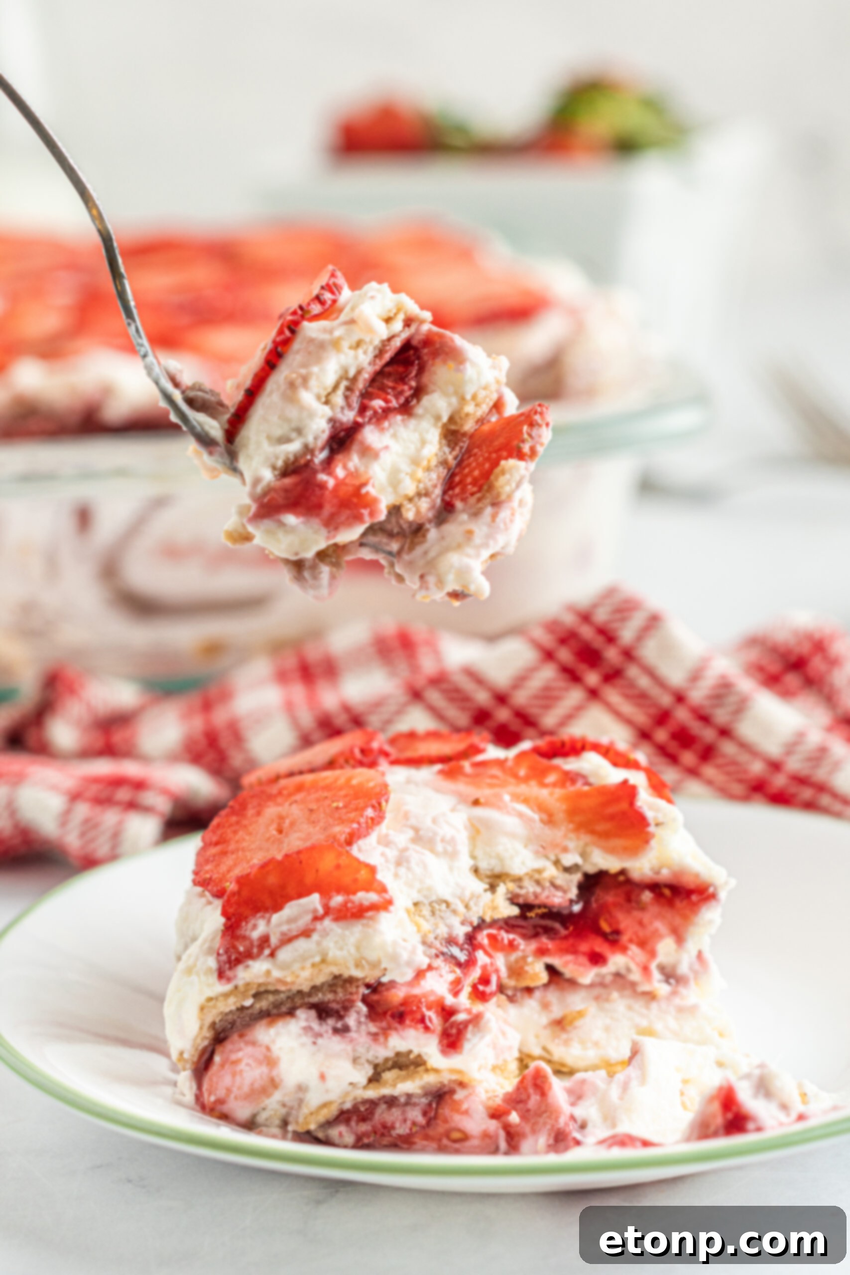 A delectable piece of Strawberry Cheesecake Icebox Cake on a white and green plate, with a silver fork delicately removing a bite, showcasing the moist interior.
