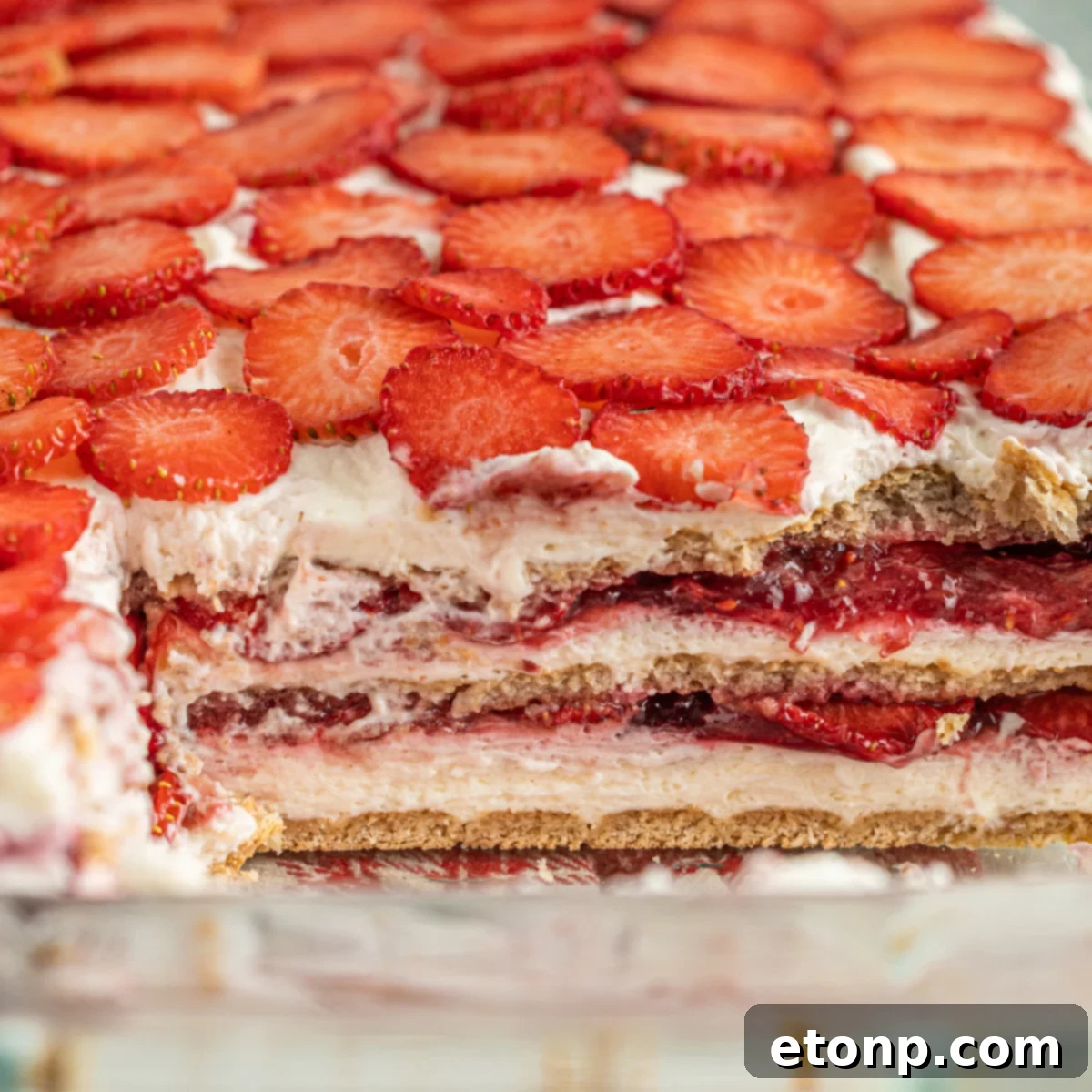 A perfectly portioned slice of Strawberry Cheesecake Icebox Cake, removed from the full cake to prominently display its inviting layers of cream, berries, and graham crackers.