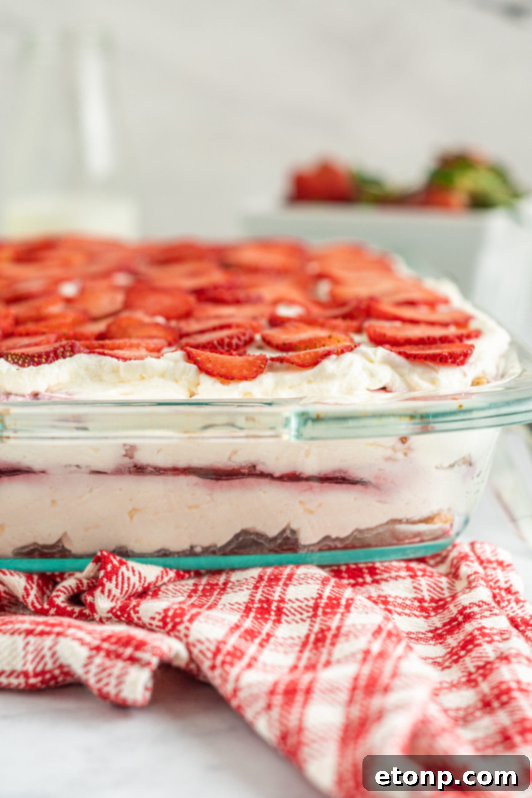 A vibrant close-up side view of the Strawberry Cheesecake Icebox Cake, revealing the rich textures of the cream, strawberries, and graham cracker layers.
