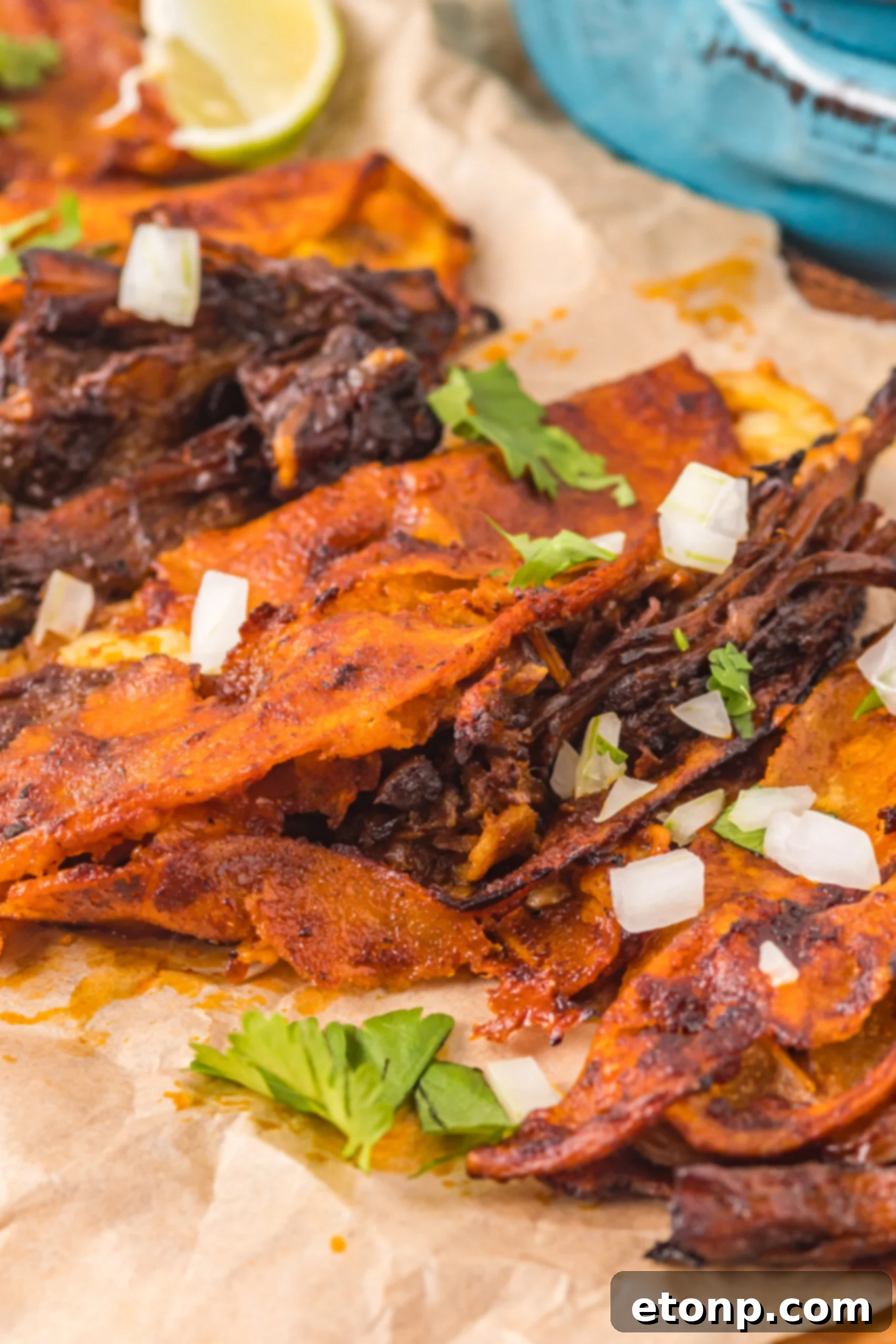 Close up view of Birria Tacos on a wooden board garnished with onion and cilantro.