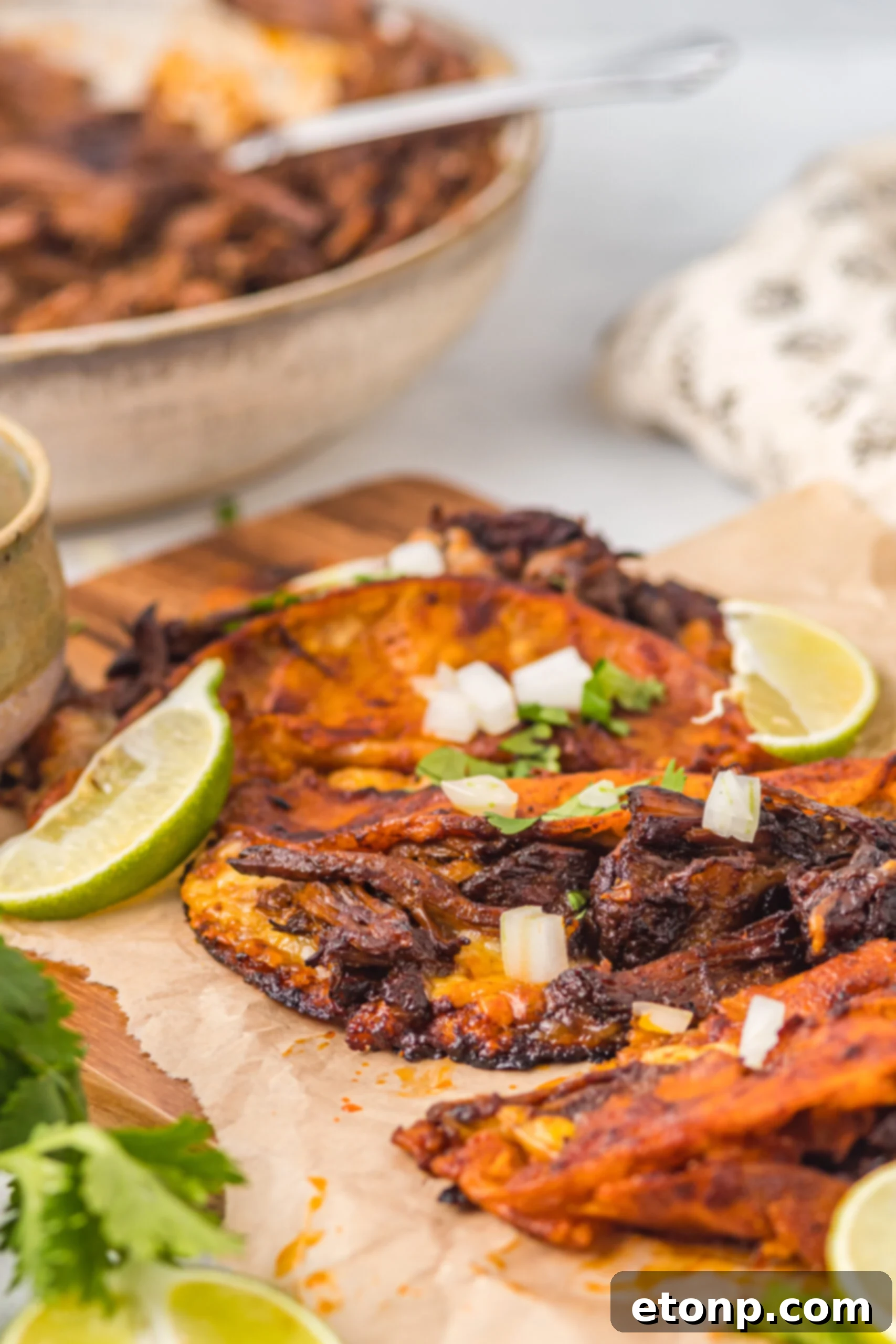 Front view of Birria Tacos on a wooden board garnished with onion and cilantro.
