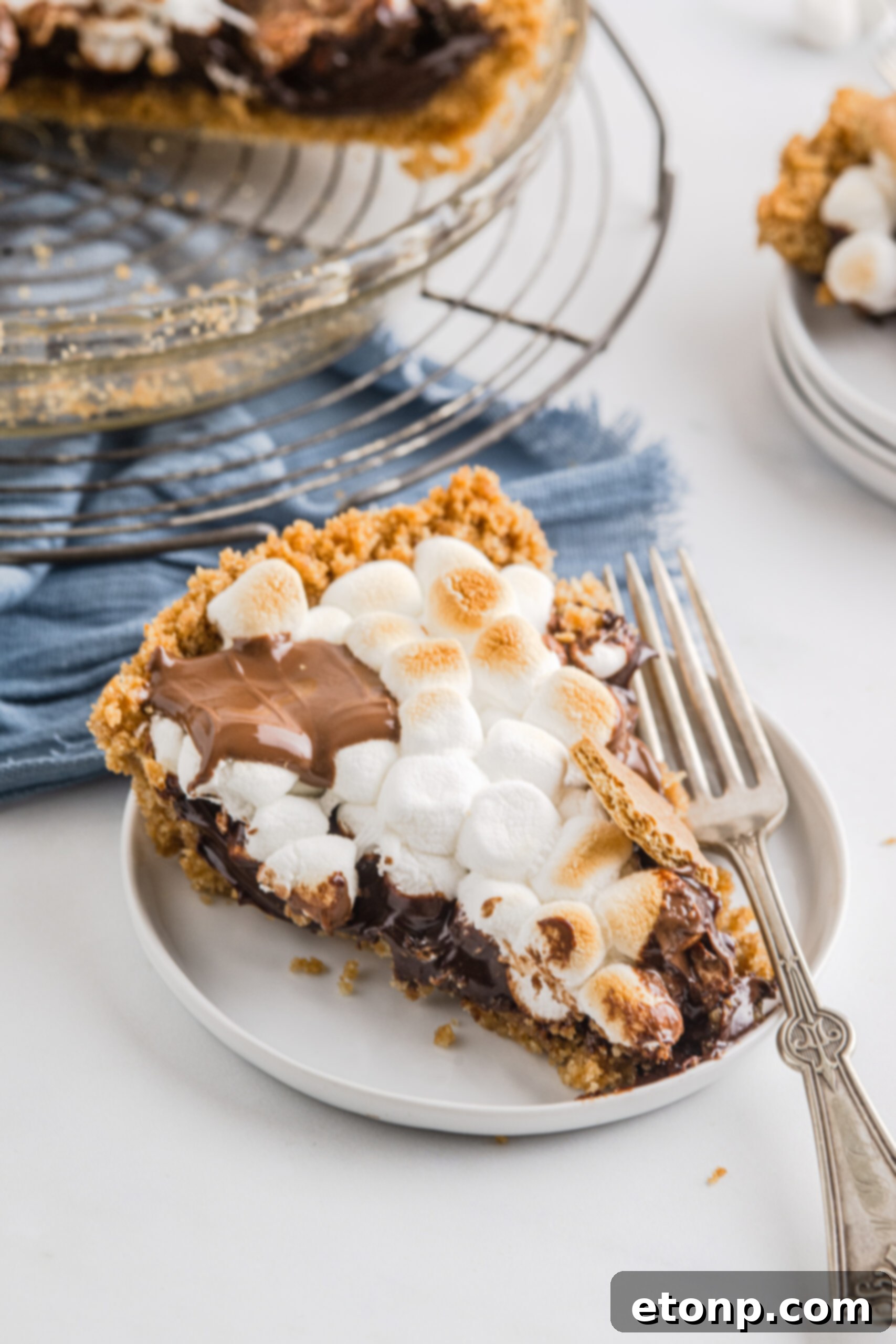 A piece of S'mores Pie on a white plate with a silver fork. 