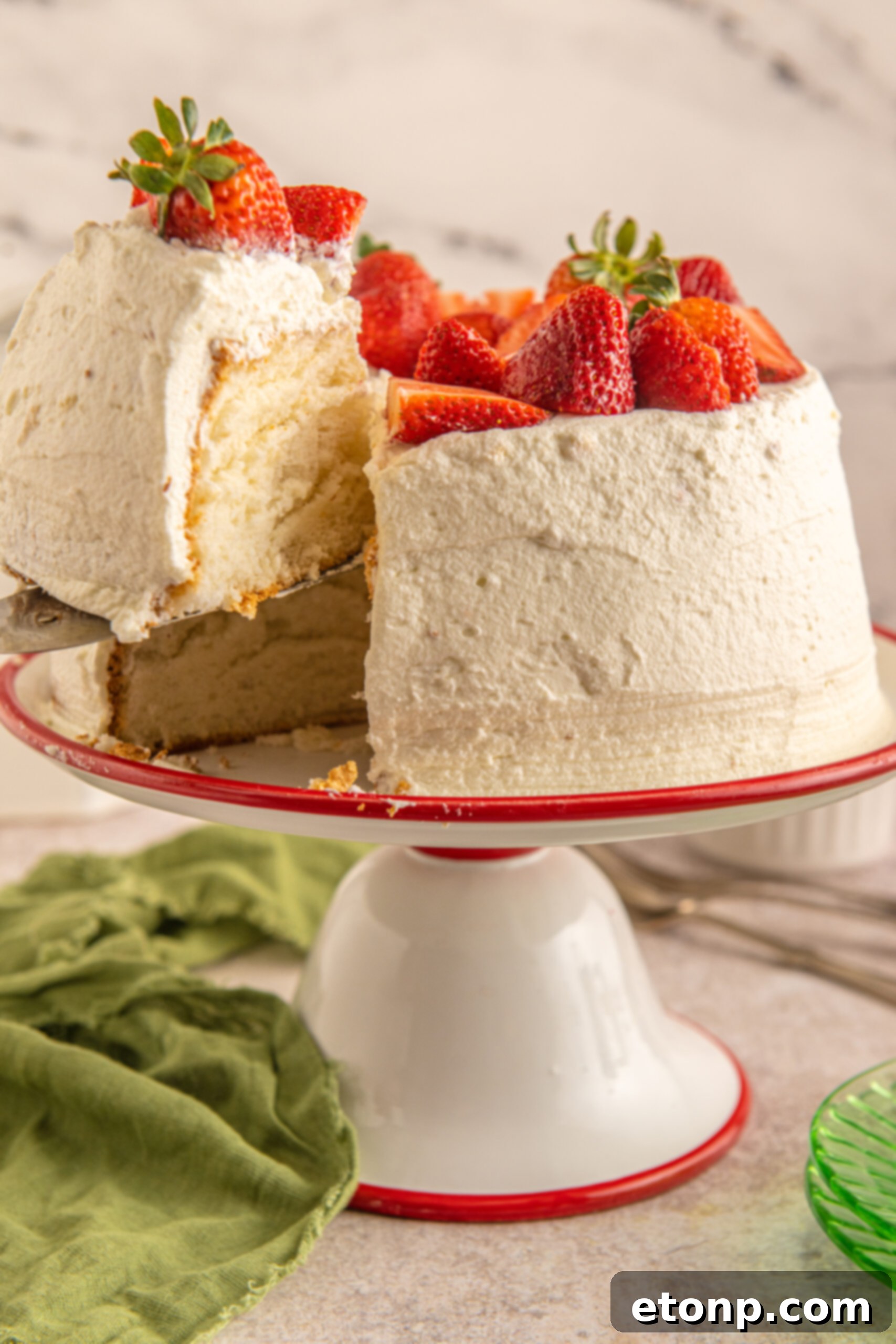 A slice of fluffy Strawberry Angel Food Cake being served from a red and white cake stand with a silver spatula, showcasing its layers.