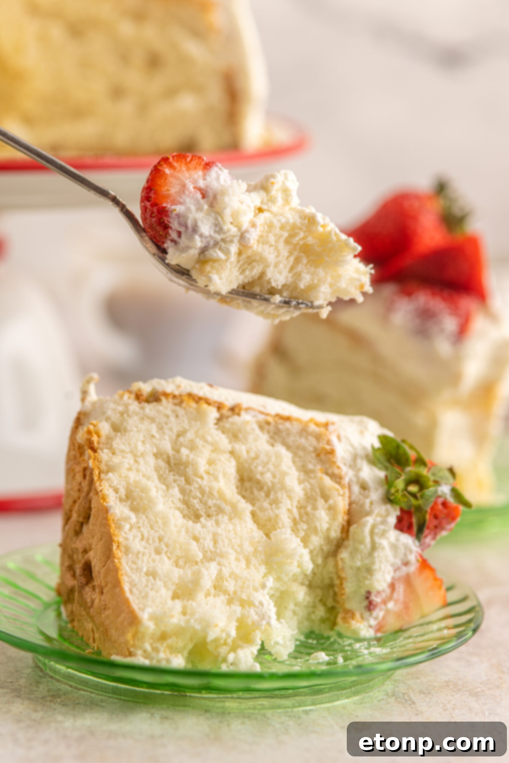A silver fork poised to take a bite from a slice of Strawberry Angel Food Cake, highlighting its delicious appeal.