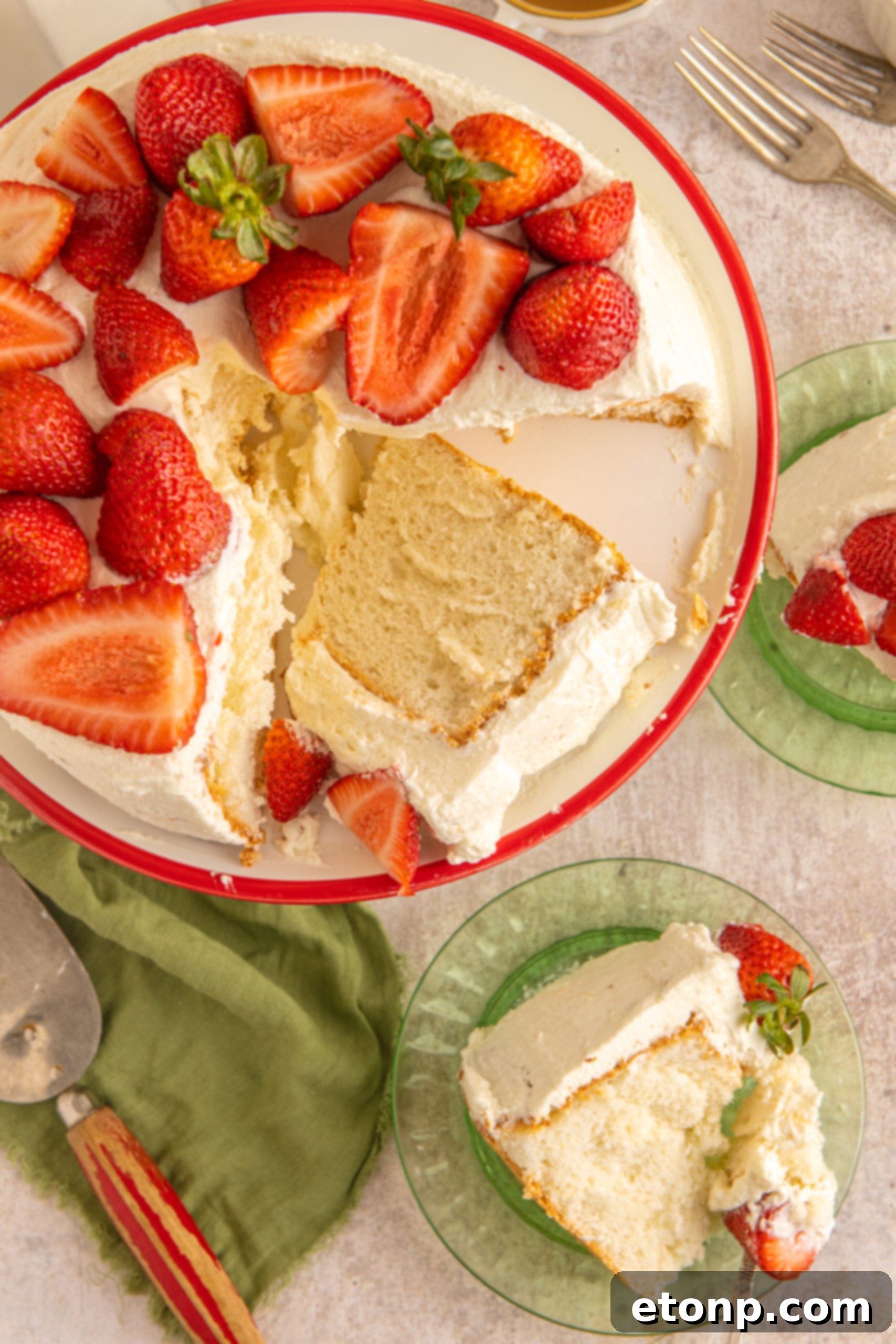 Overhead view of a beautiful Strawberry Angel Food Cake on a white and red cake stand, with two individual servings on green plates in the background.