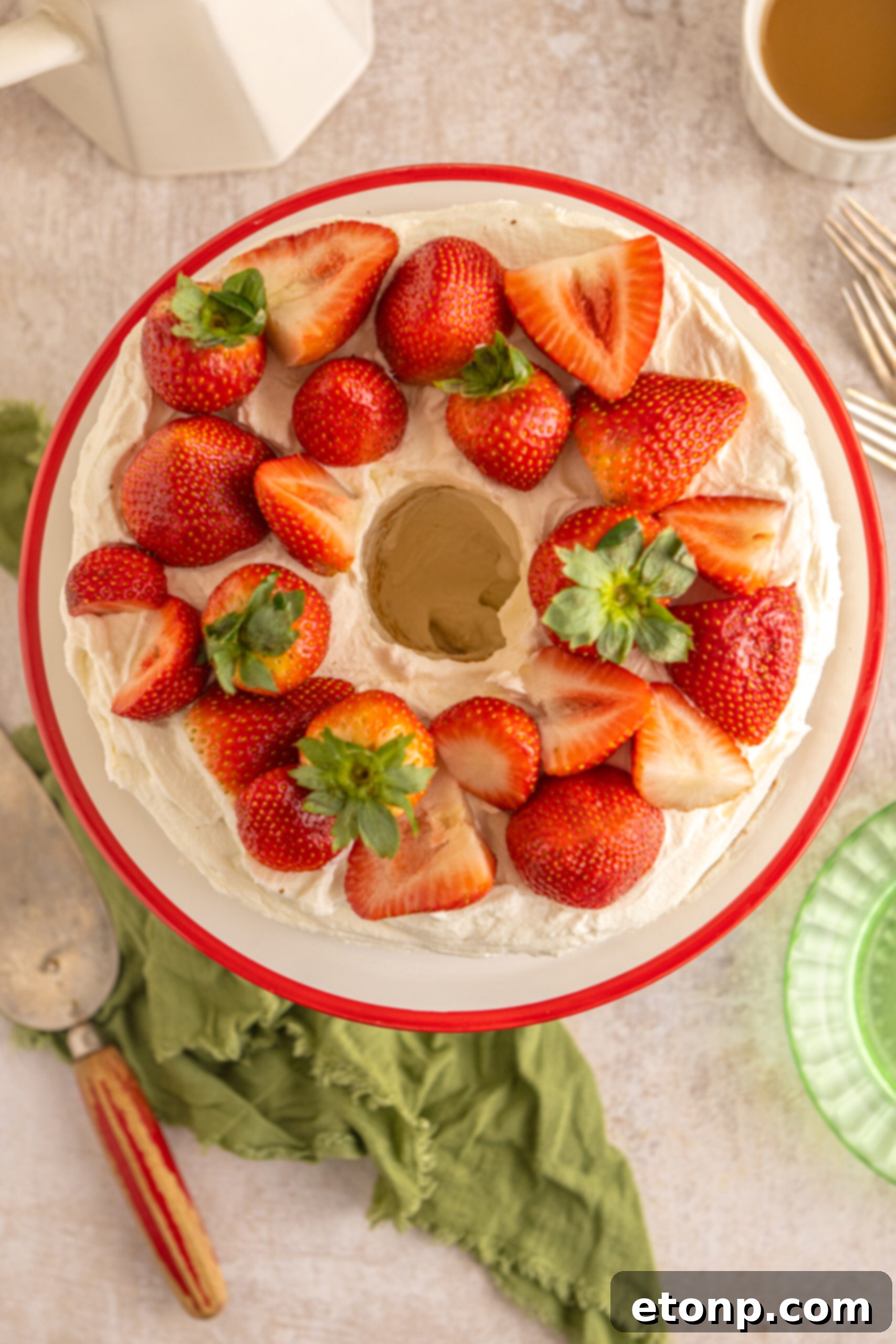 Overhead perspective of the complete Strawberry Angel Food Cake, generously adorned with bright red fresh strawberries, ready to be sliced.