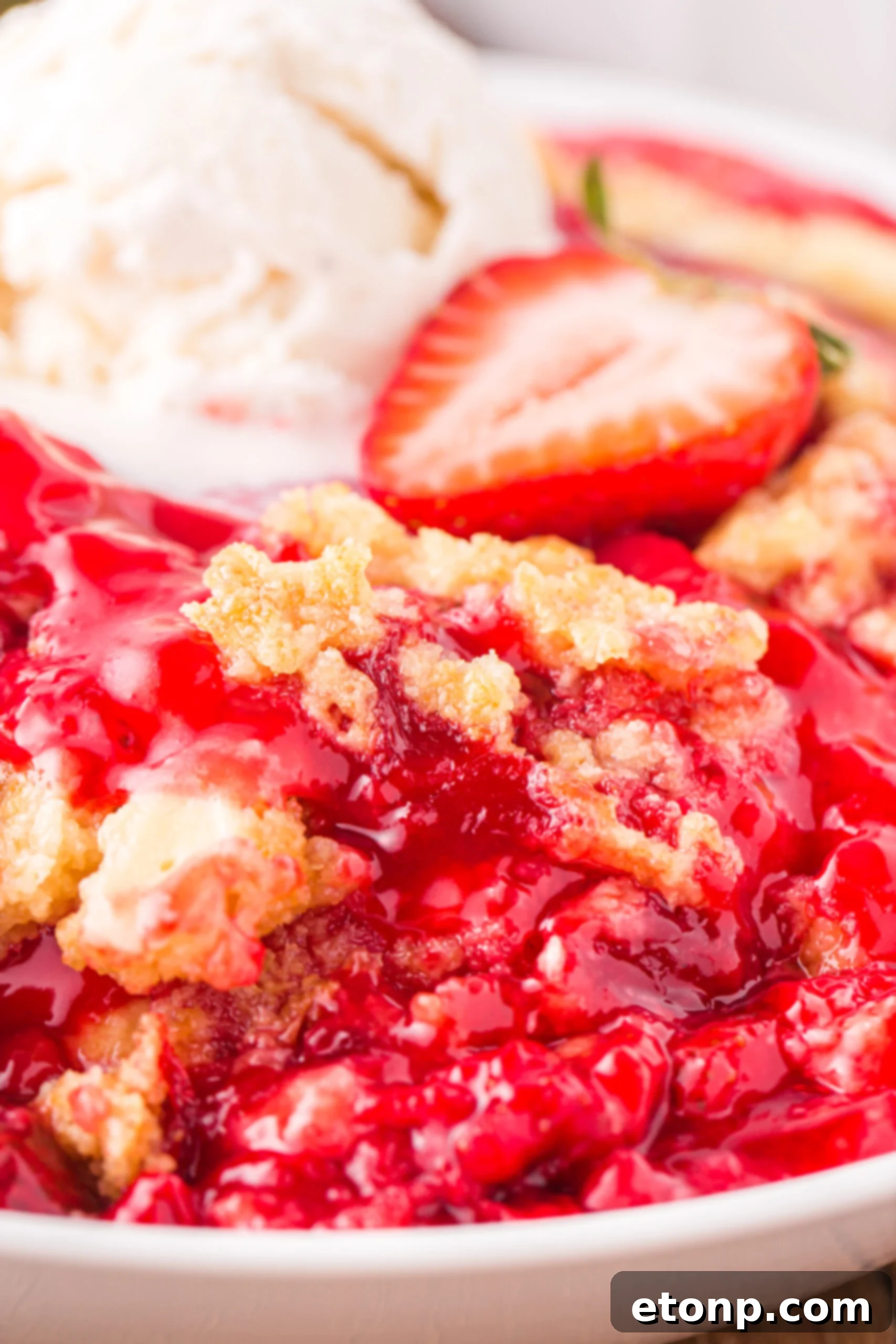 Close up view of a serving of Strawberry Dump Cake in a white bowl topped with a scoop of ice cream.