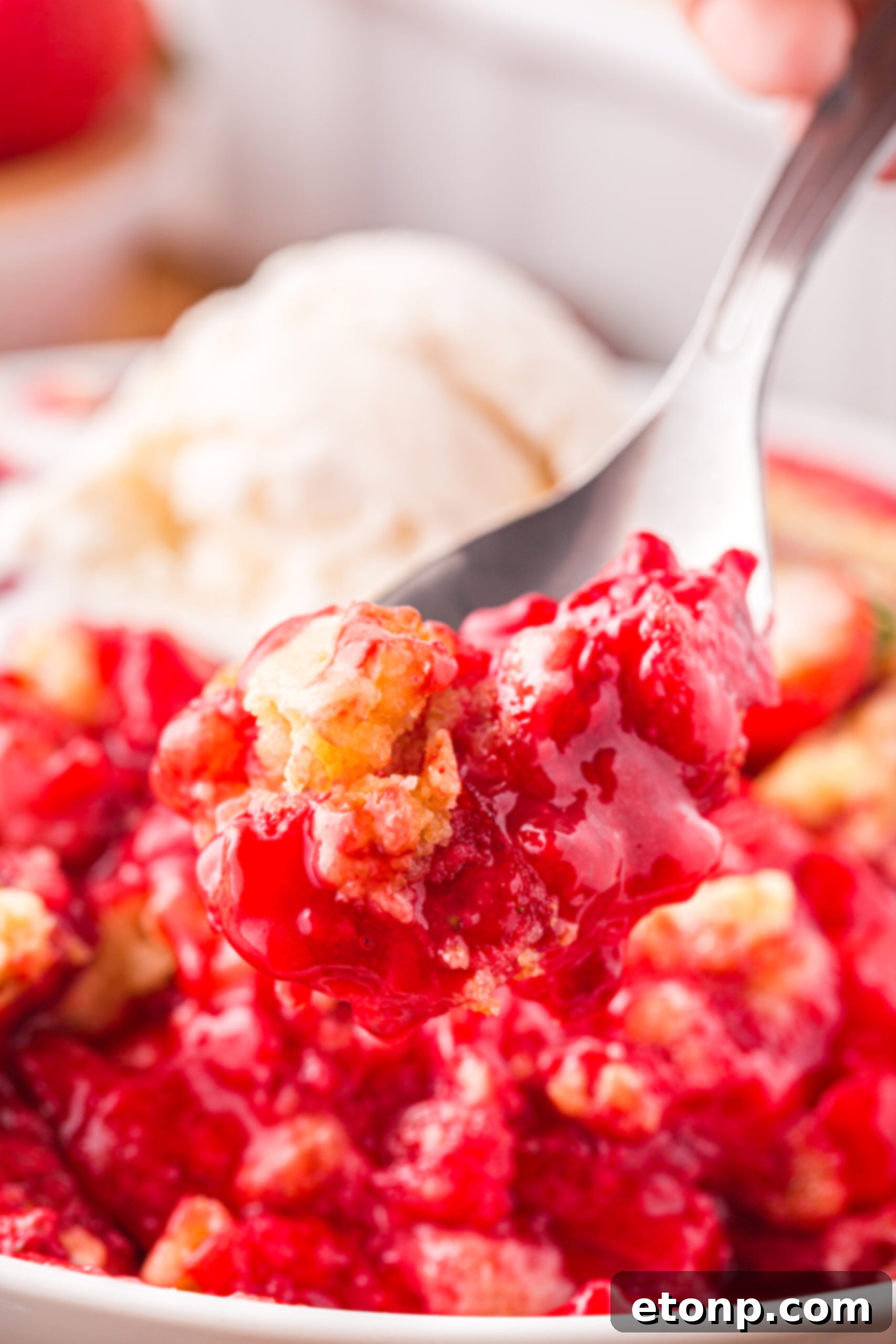 Close up view of a bite of Strawberry Dump Cake on a silver spoon.