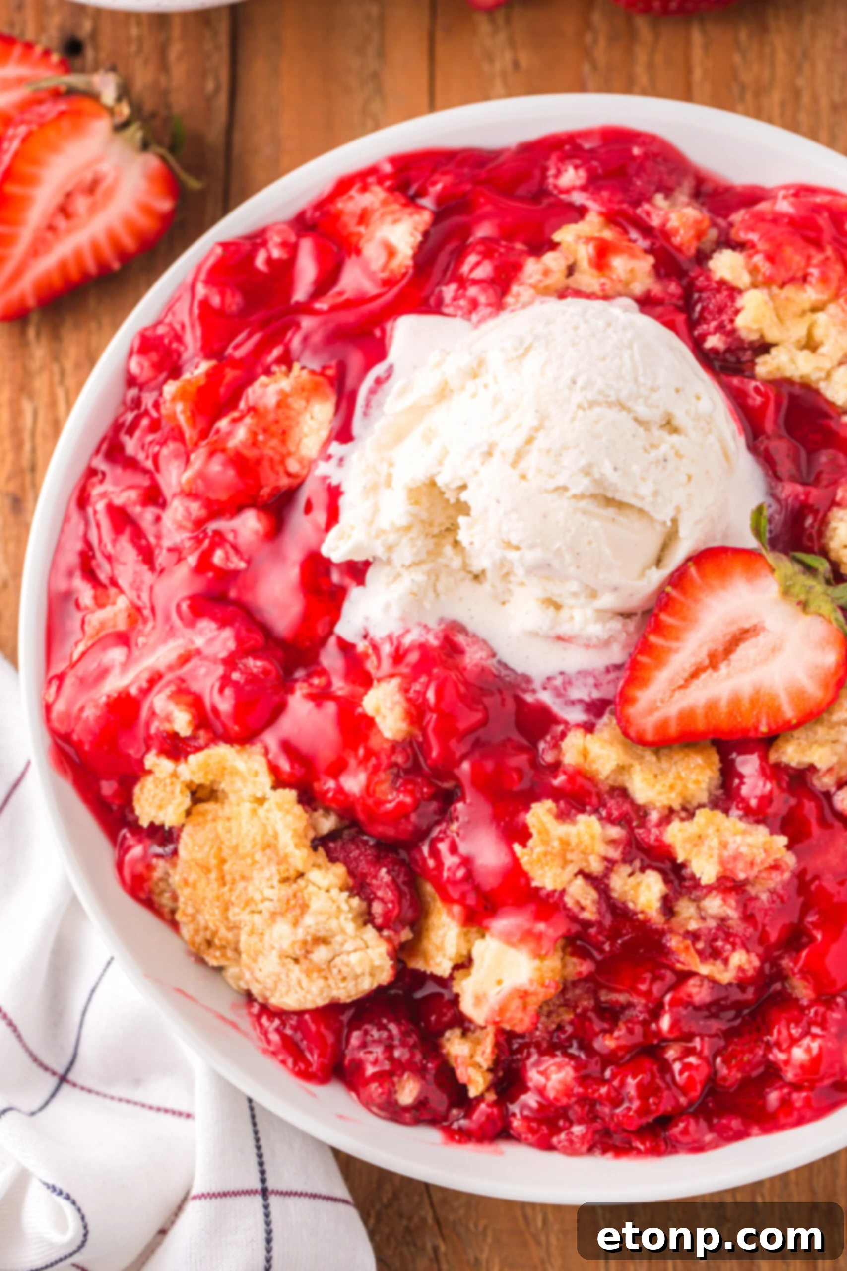 overhead view of a serving of Strawberry Dump Cake in a white bowl topped with a scoop of ice cream.