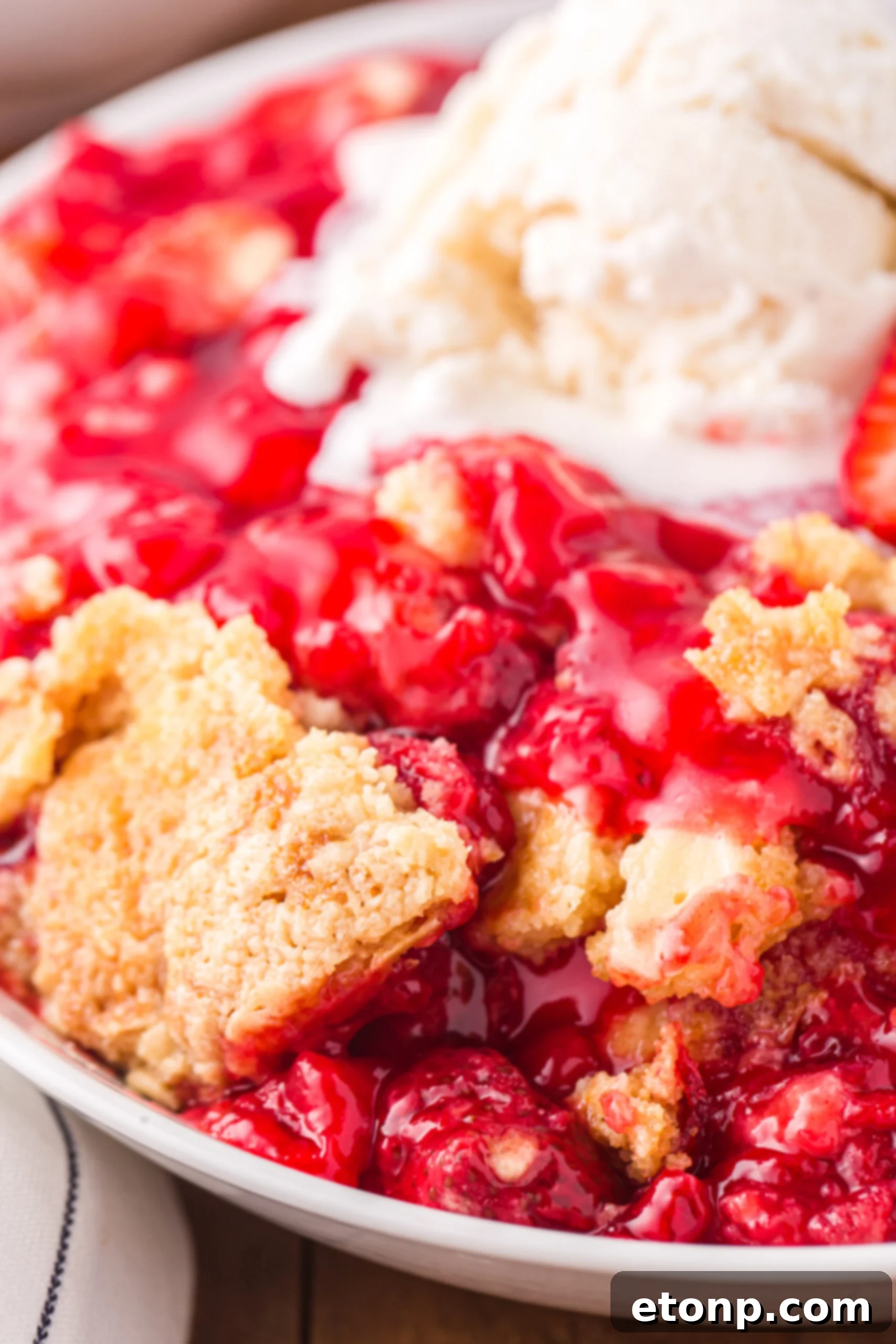Close up view of a serving of Strawberry Dump Cake in a white bowl topped with a scoop of ice cream.