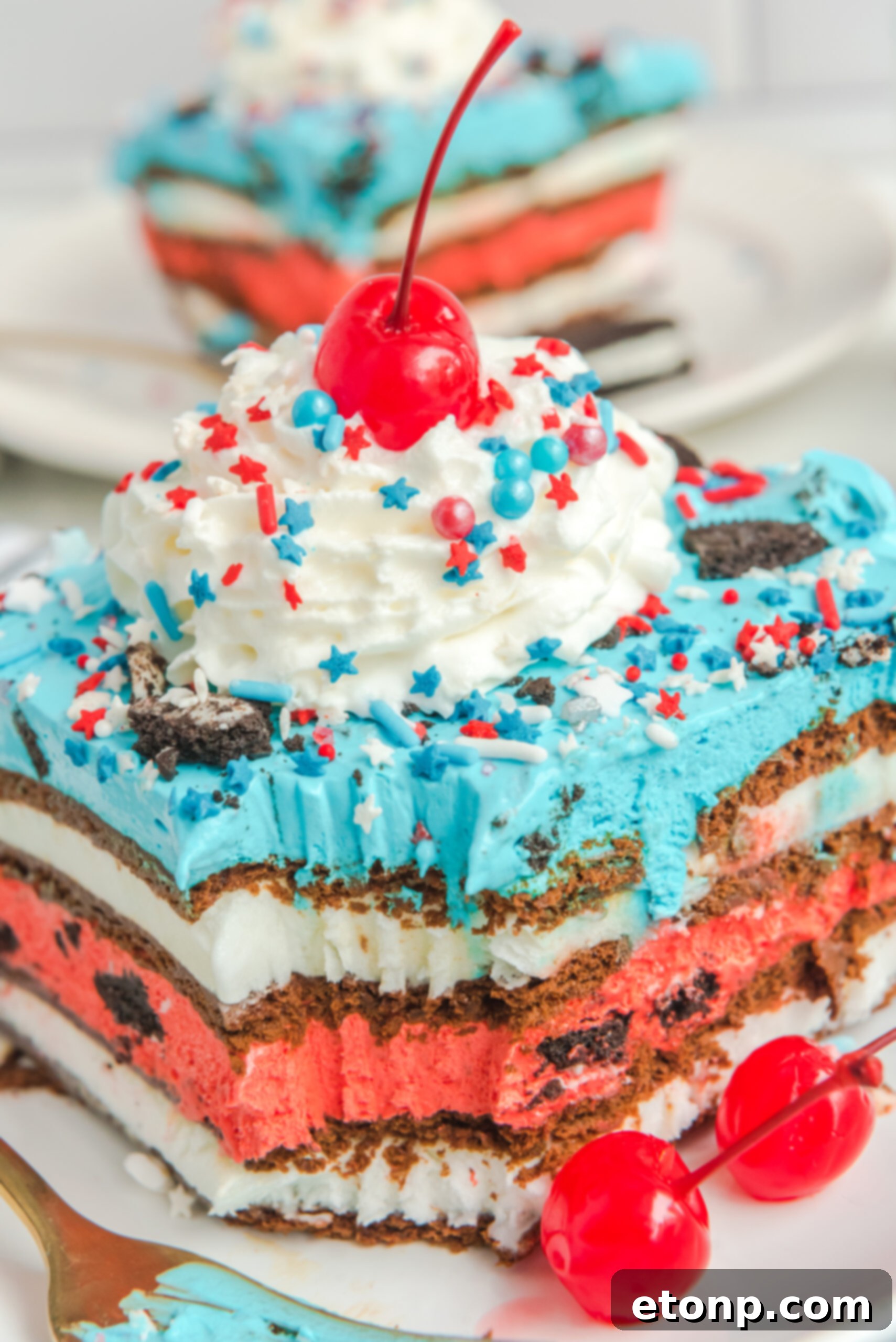 Overhead view of a slice of Patriotic Ice Cream Sandwich Cake topped with whipped cream and cherry.