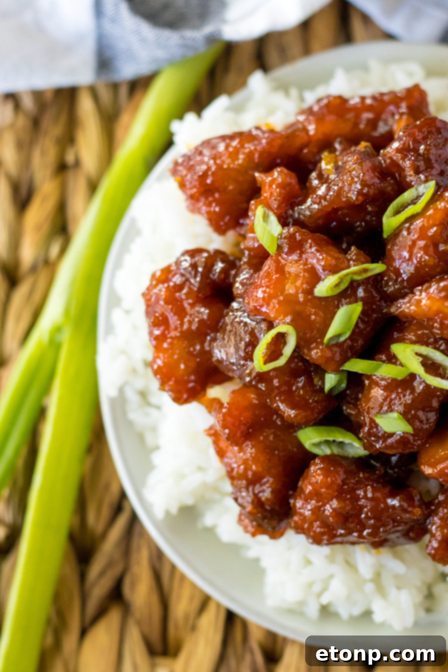 Close-up view of Slow Cooker Firecracker Chicken over white rice in a white bowl, showing the texture of the chicken and sauce.