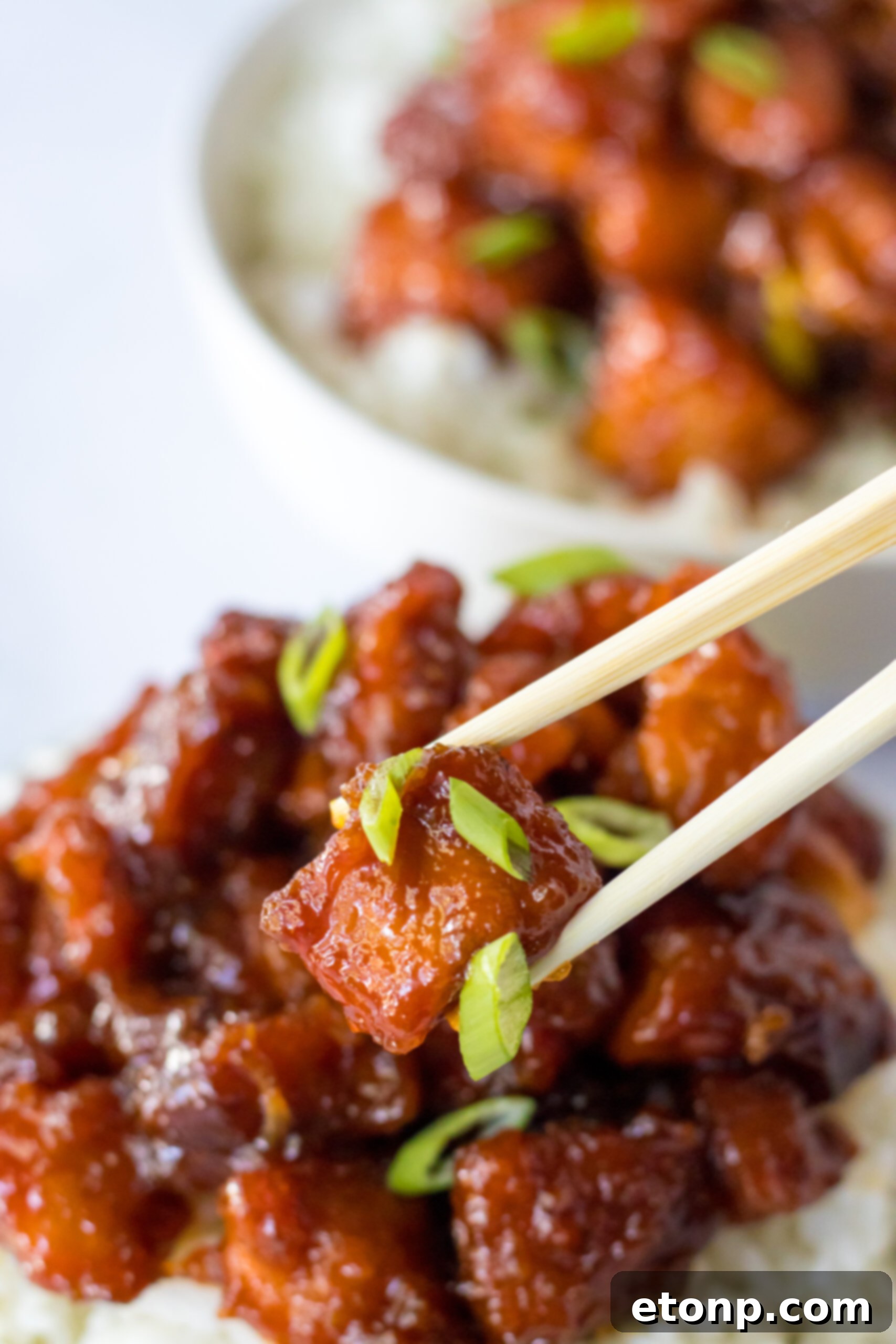 Close-up view of chopsticks holding a perfectly glazed piece of Slow Cooker Firecracker Chicken, ready to be enjoyed.