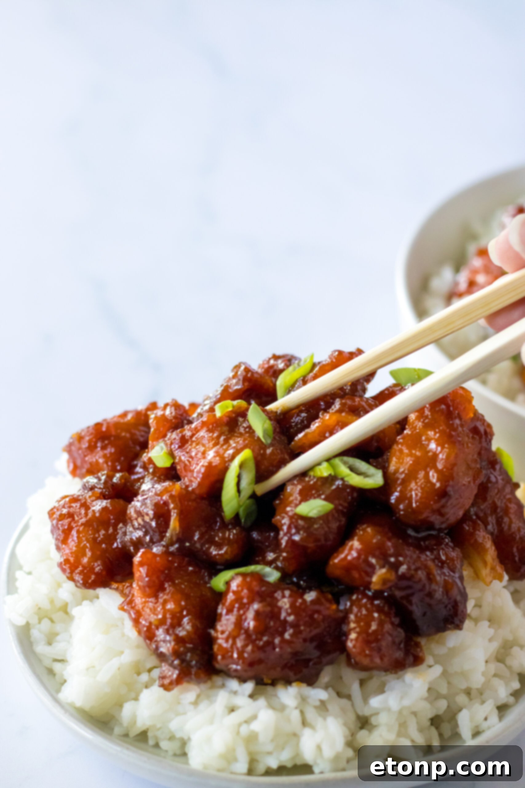 Close-up view of chopsticks holding a saucy piece of Slow Cooker Firecracker Chicken, emphasizing the texture and glaze.