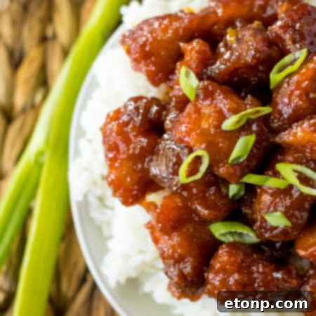 Slow Cooker Firecracker Chicken in a white bowl over rice, garnished with scallions.
