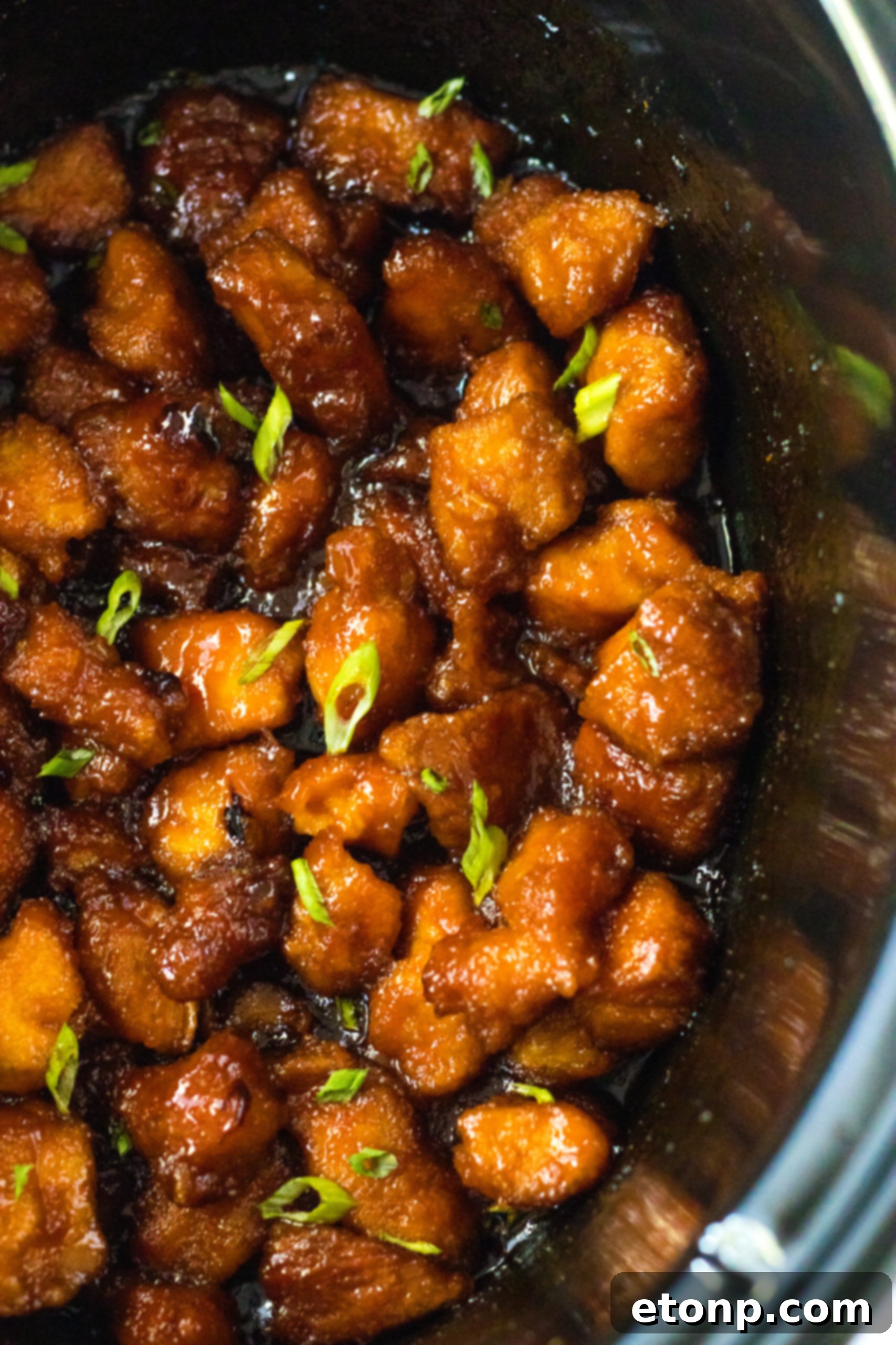 Close-up overhead view of Slow Cooker Firecracker Chicken simmering gently in a crock pot, showcasing the rich, vibrant sauce.