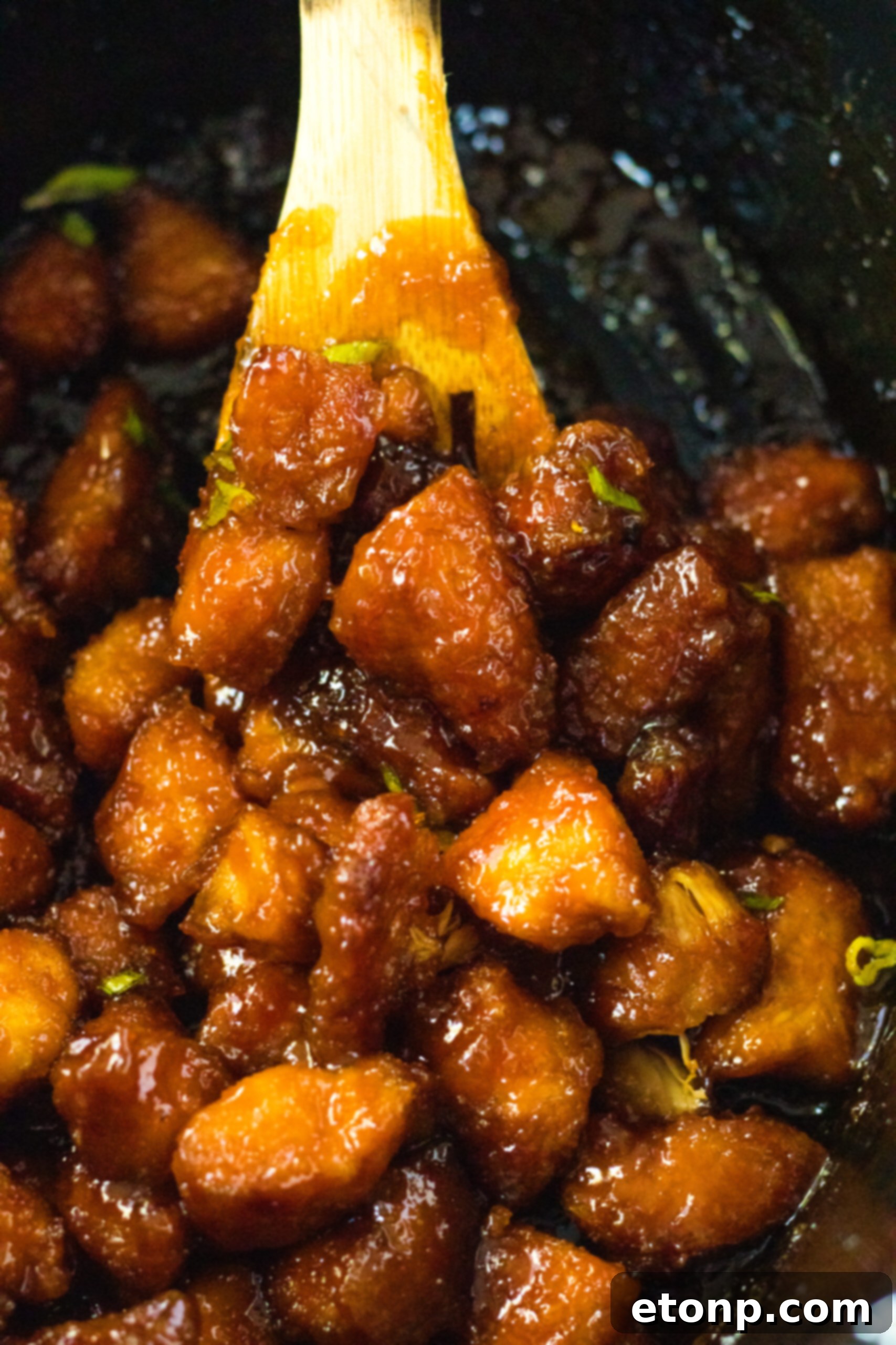 A wooden spoon carefully removing a generous serving of Slow Cooker Firecracker Chicken from the crock pot, highlighting the saucy chicken pieces.