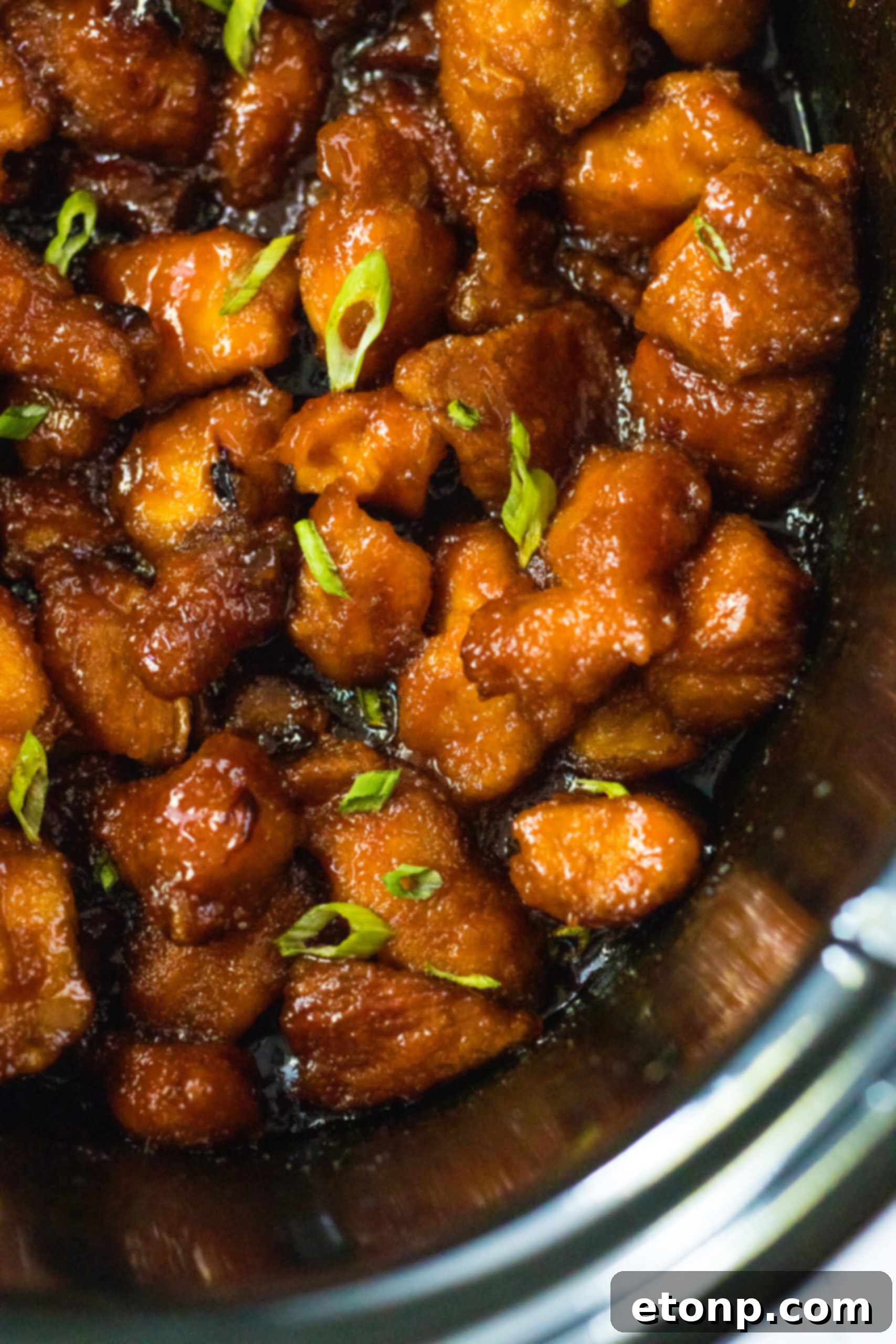 A close-up view of succulent Slow Cooker Firecracker Chicken pieces bathed in a rich, sweet, and spicy sauce within a slow cooker.