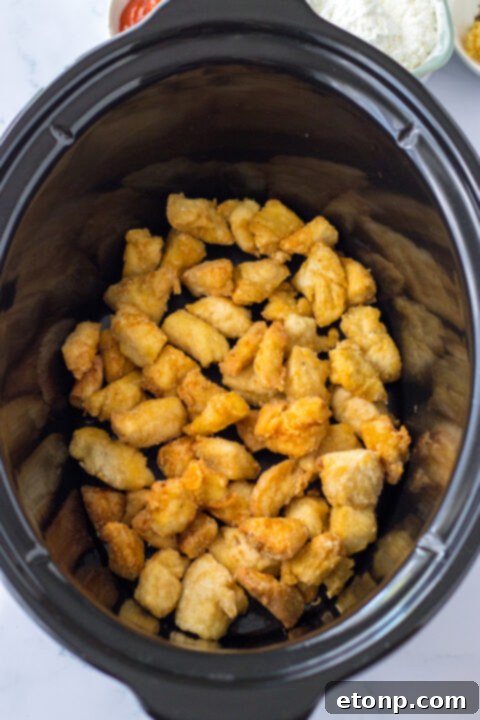 Browning chicken pieces being transferred from the skillet to a slow cooker.
