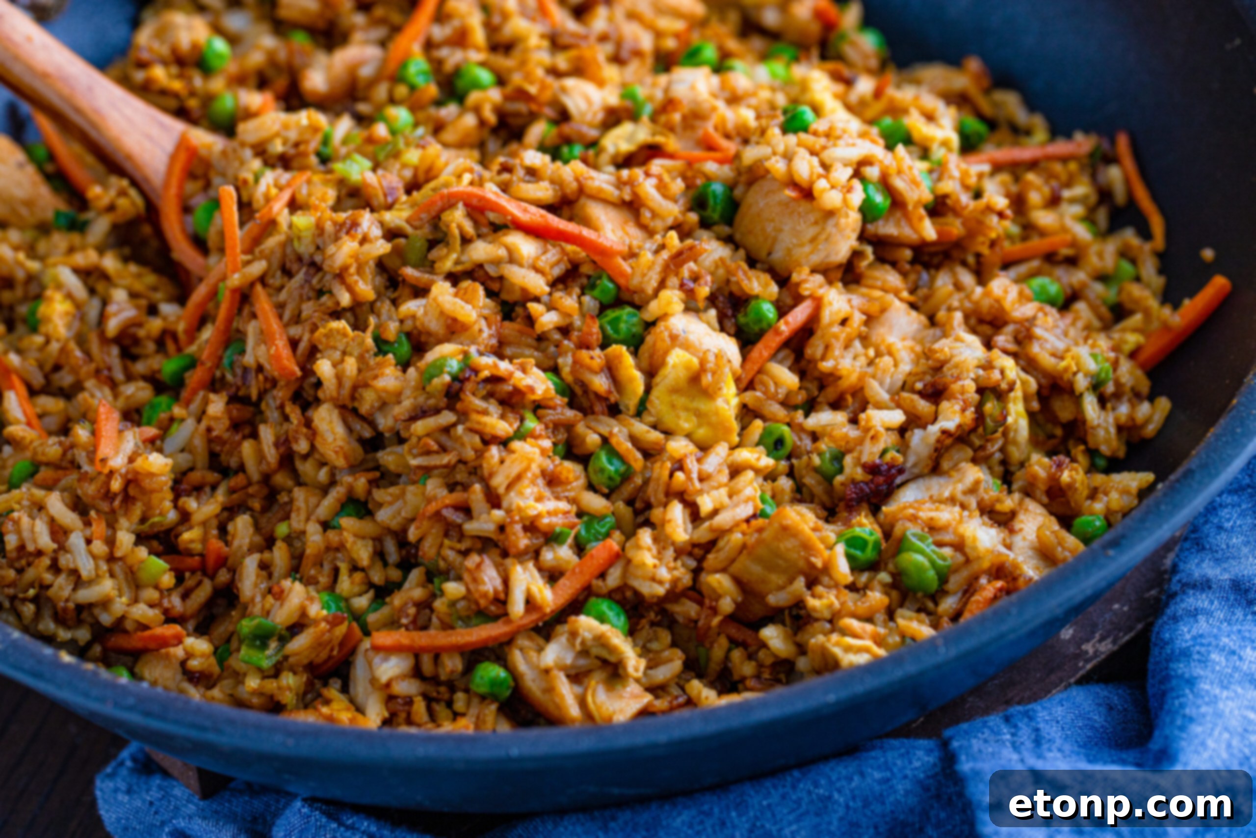 A large skillet filled with chicken fried rice, with a wooden spoon resting in it, ready to serve.