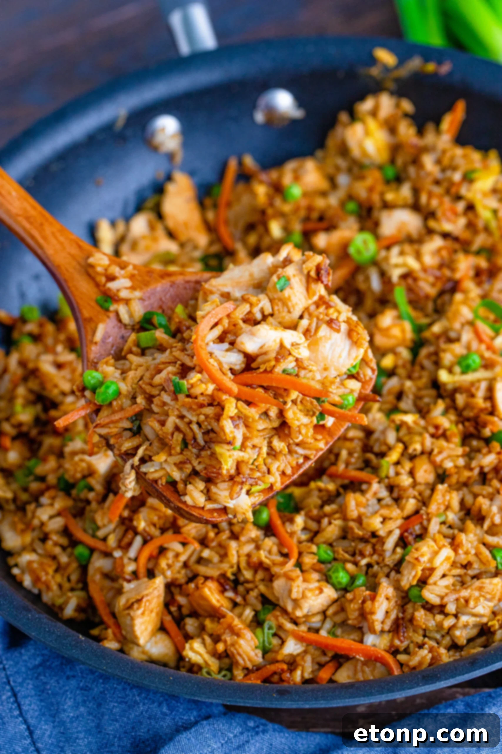 A close-up shot of a spoon scooping a portion of chicken fried rice, showing chicken, rice, and vegetables.