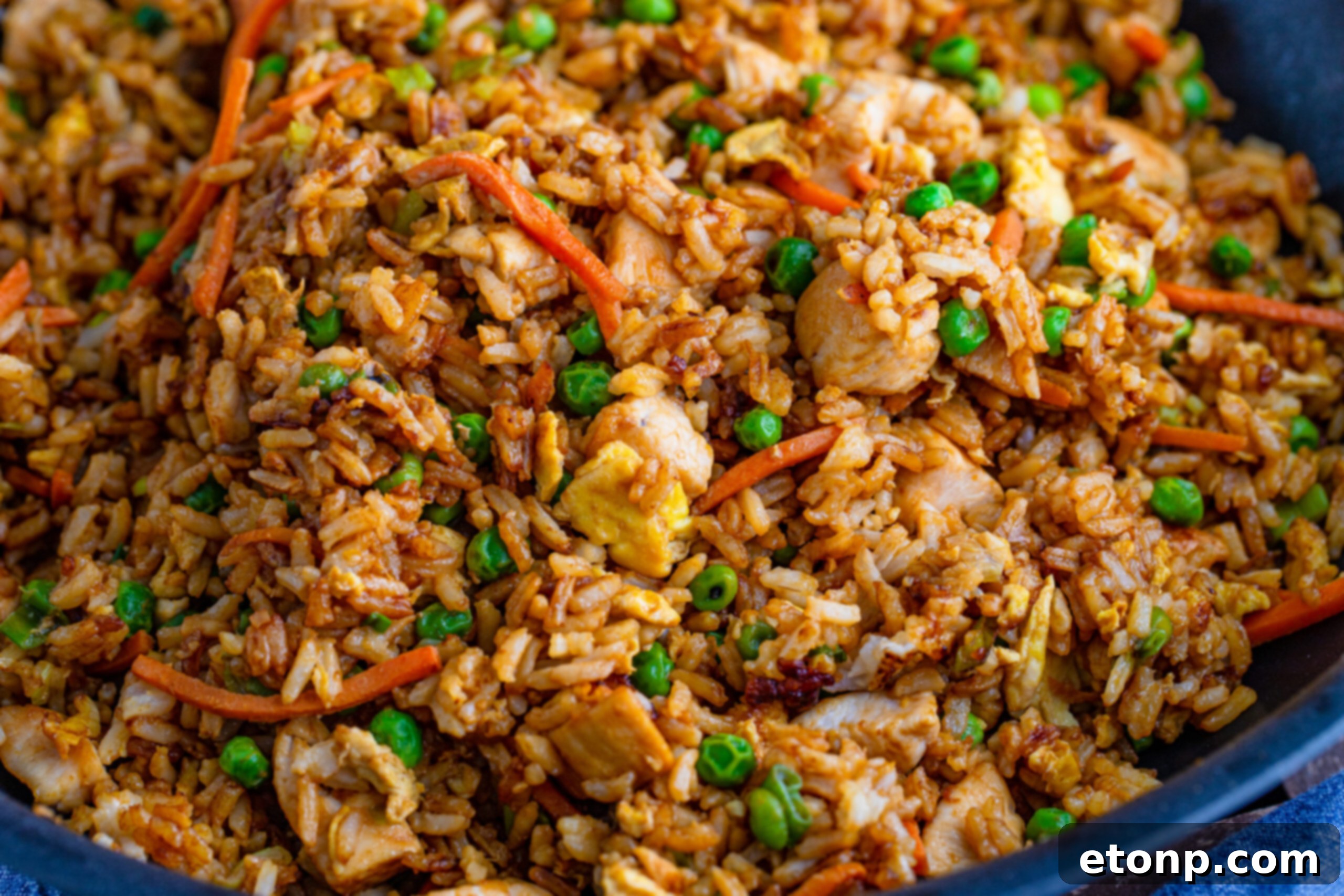 An overhead view of chicken fried rice cooking in a large skillet, showing rice, chicken, eggs, and mixed vegetables.