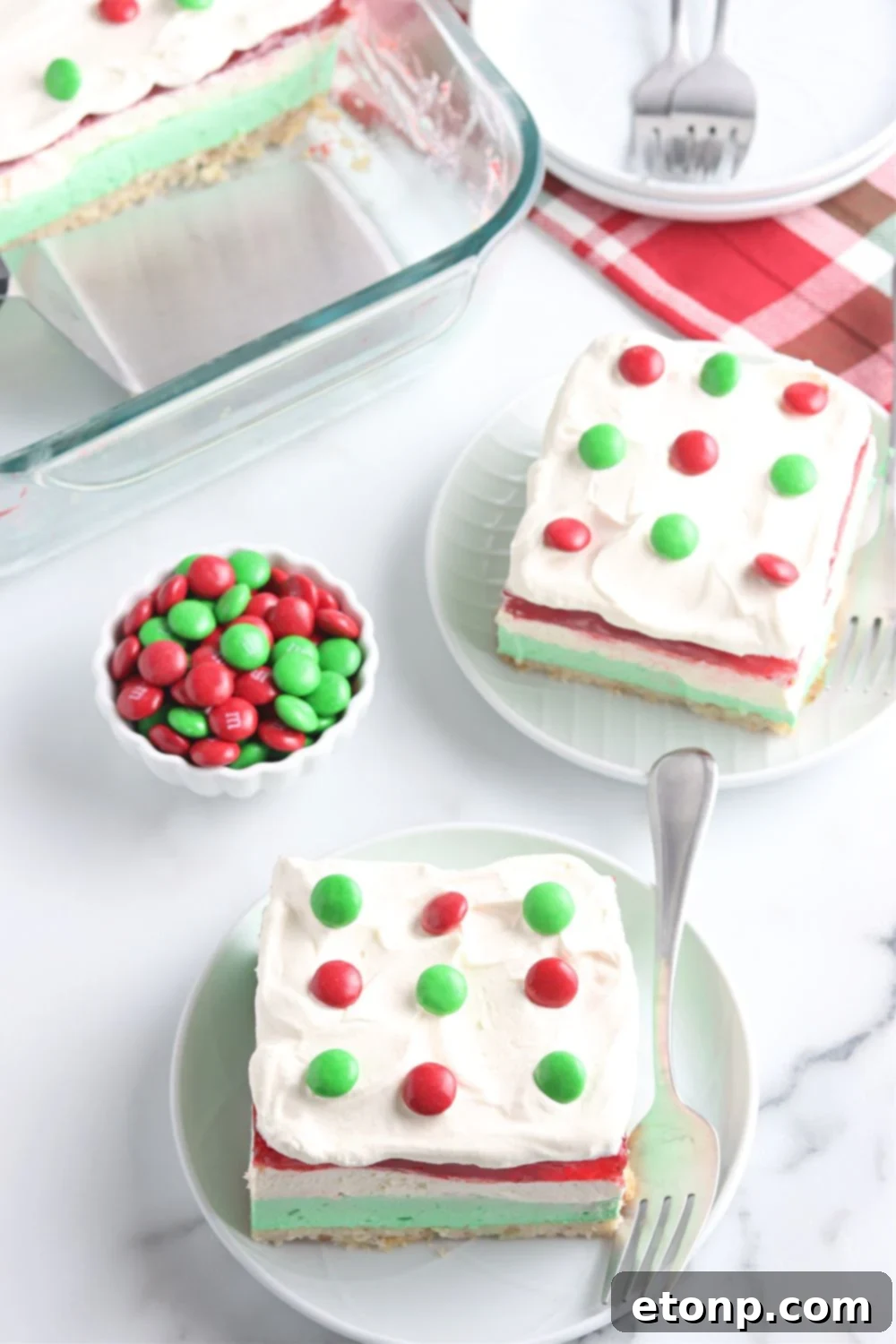 Plates adorned with slices of Christmas dessert lasagna are artfully arranged on a table, accompanied by a bowl of festive red and green M&Ms, adding a playful holiday touch.