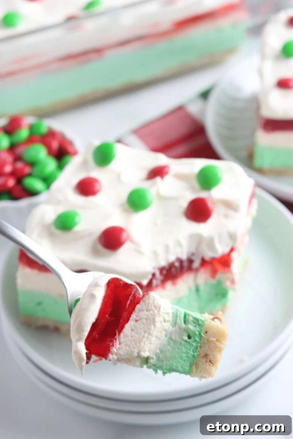 A fork lifts a festive bite of the Christmas dessert lasagna, delicately balanced above a white plate, ready to be enjoyed.