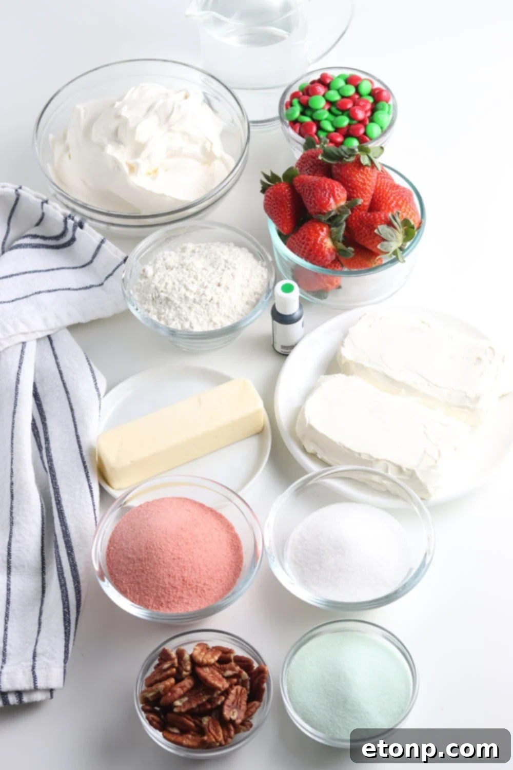 Various ingredients for a layered Christmas dessert are neatly arranged in small bowls on a rustic wooden table, ready for preparation.
