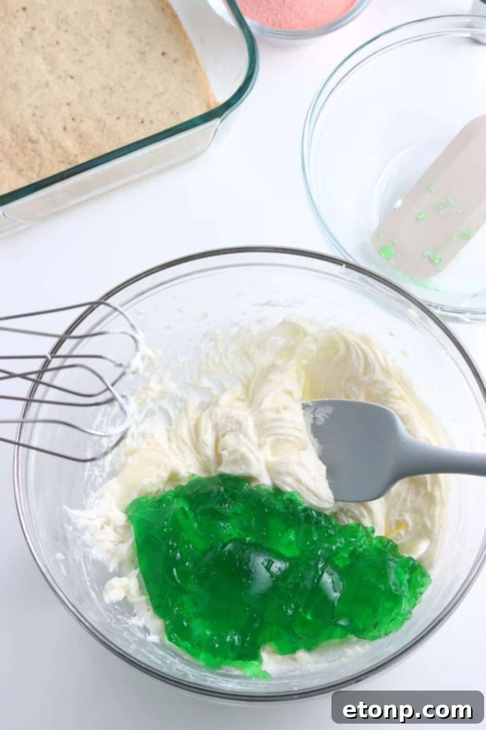 A glass bowl contains a vibrant green jello mixture, lightened and made creamy with the addition of whipped cream, for the first layer of the dessert.