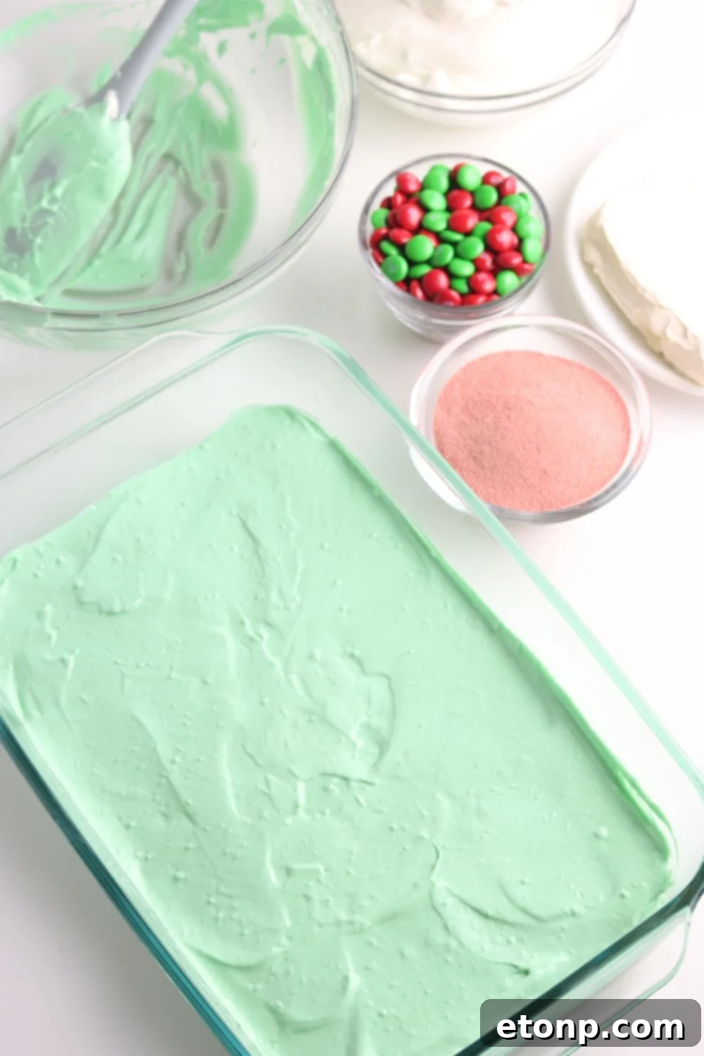 The green jello and cream cheese mixture, the first vibrant layer of the Christmas dessert lasagna, is evenly spread in a 9x13 inch baking pan.