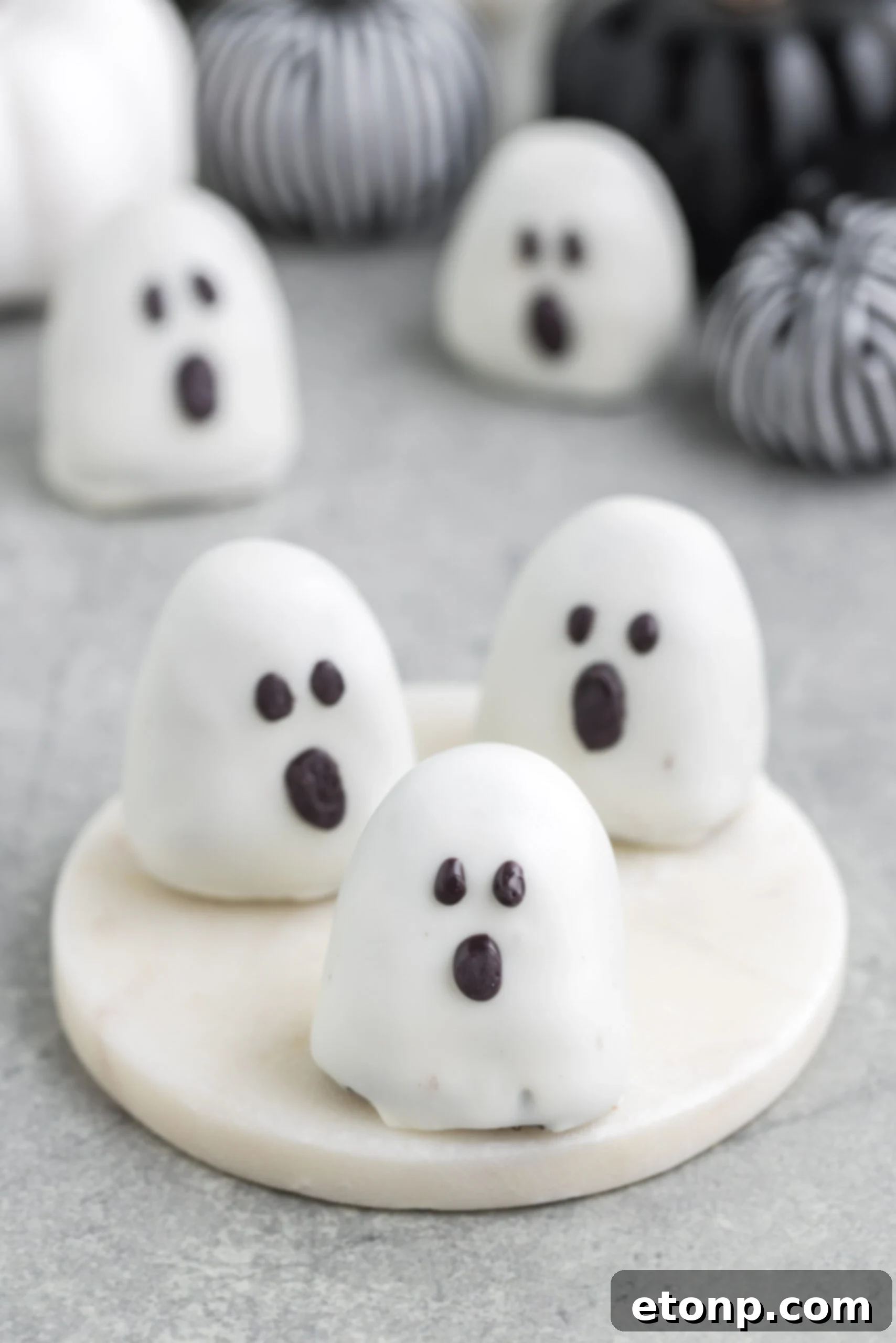 Spooky Oreo truffles arranged on a table with festive fabric pumpkins in the background, creating a warm and inviting autumn scene.