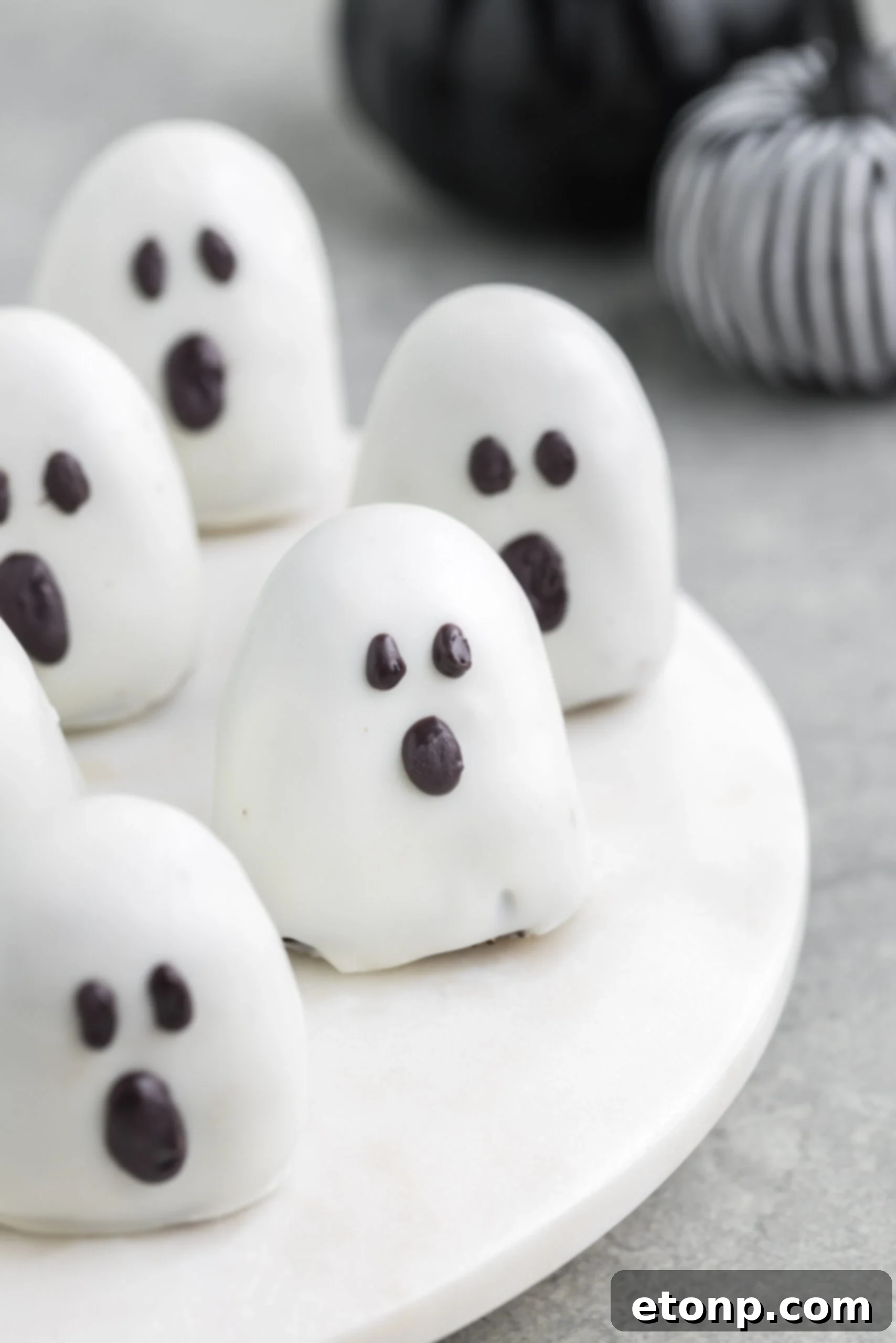 A collection of spooky Oreo truffles artfully arranged on a white marble serving platter, with autumnal fabric pumpkins adding to the festive atmosphere.