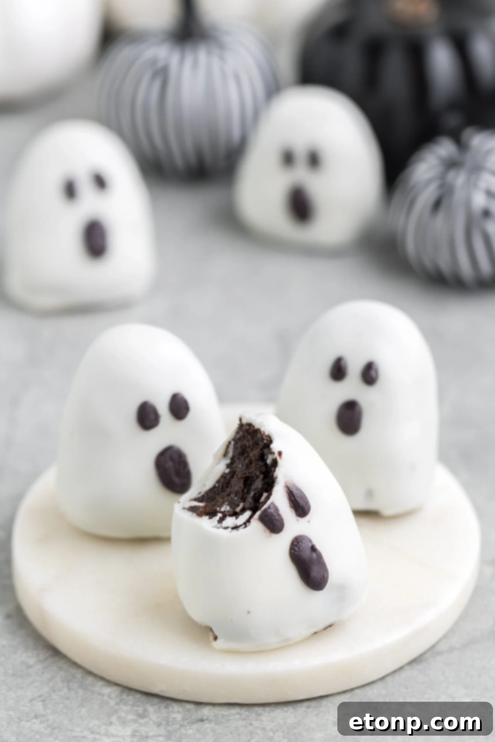 A delightful Oreo ghost truffle with a bite taken out, showcasing its creamy filling, placed invitingly on a platter atop a rustic table.