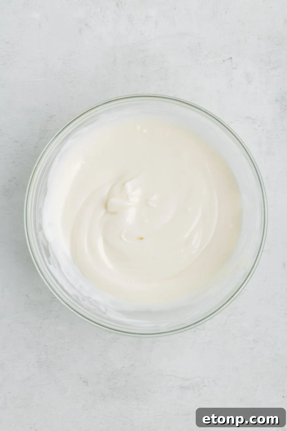 A glass bowl filled with smoothly melted white candy melts, shimmering and ready for dipping the ghost truffles.