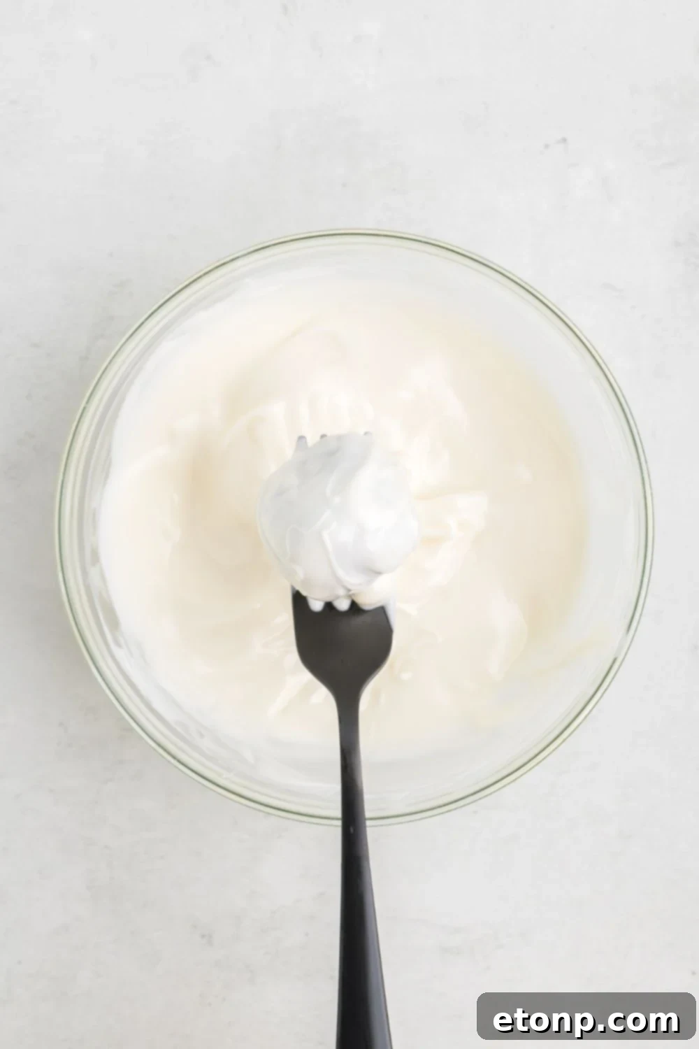 An Oreo ball being carefully dipped into melted white chocolate, held delicately with a fork above the bowl.
