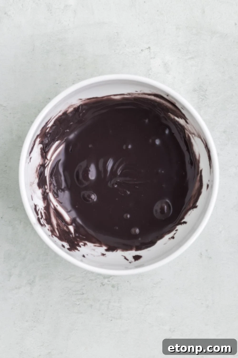 A small white bowl containing melted black candy melts, perfectly prepared for adding intricate facial features to the ghost truffles.