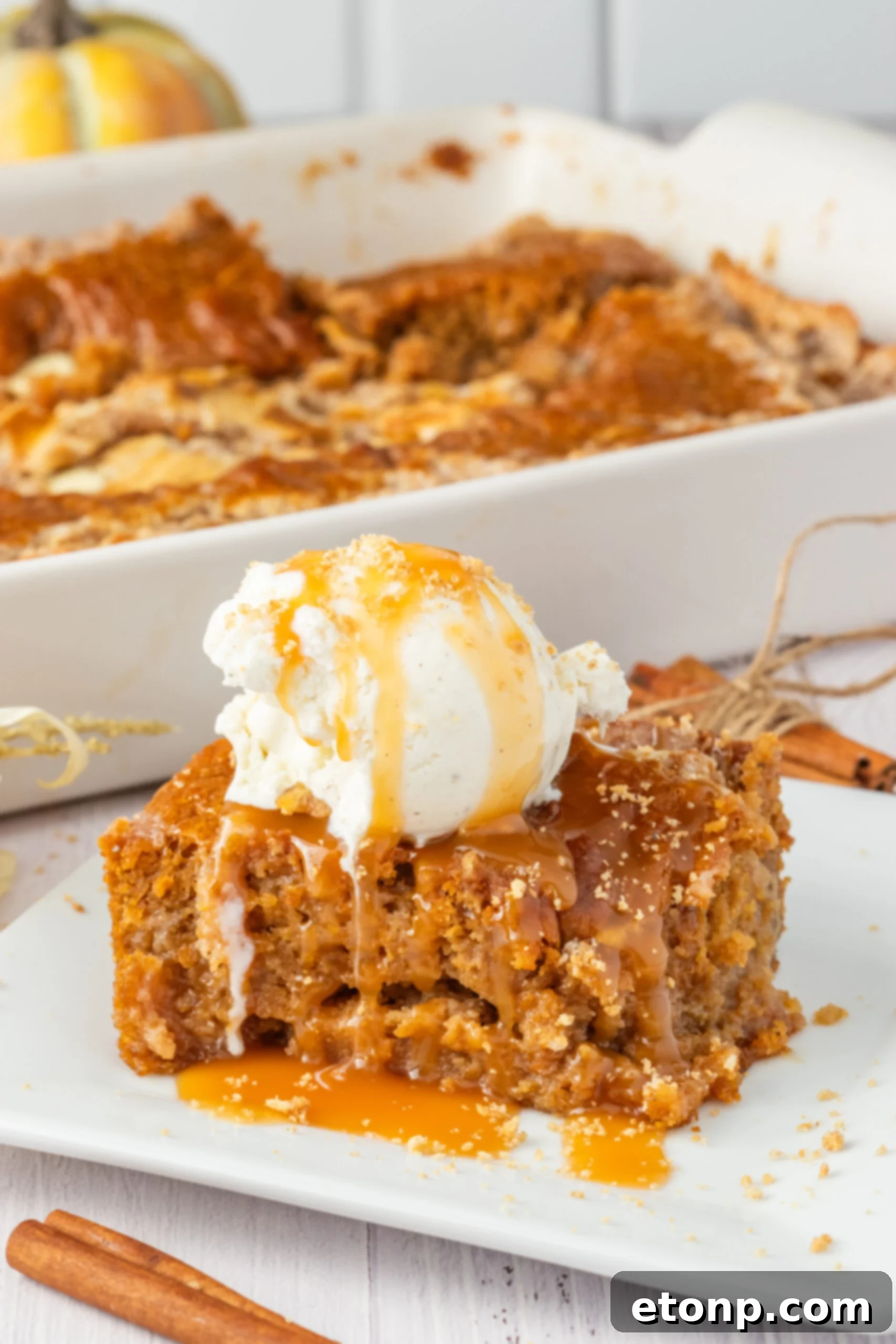 Pumpkin Earthquake Cake on a white plate with a scoop of vanilla ice cream on top then drizzled with caramel sauce
