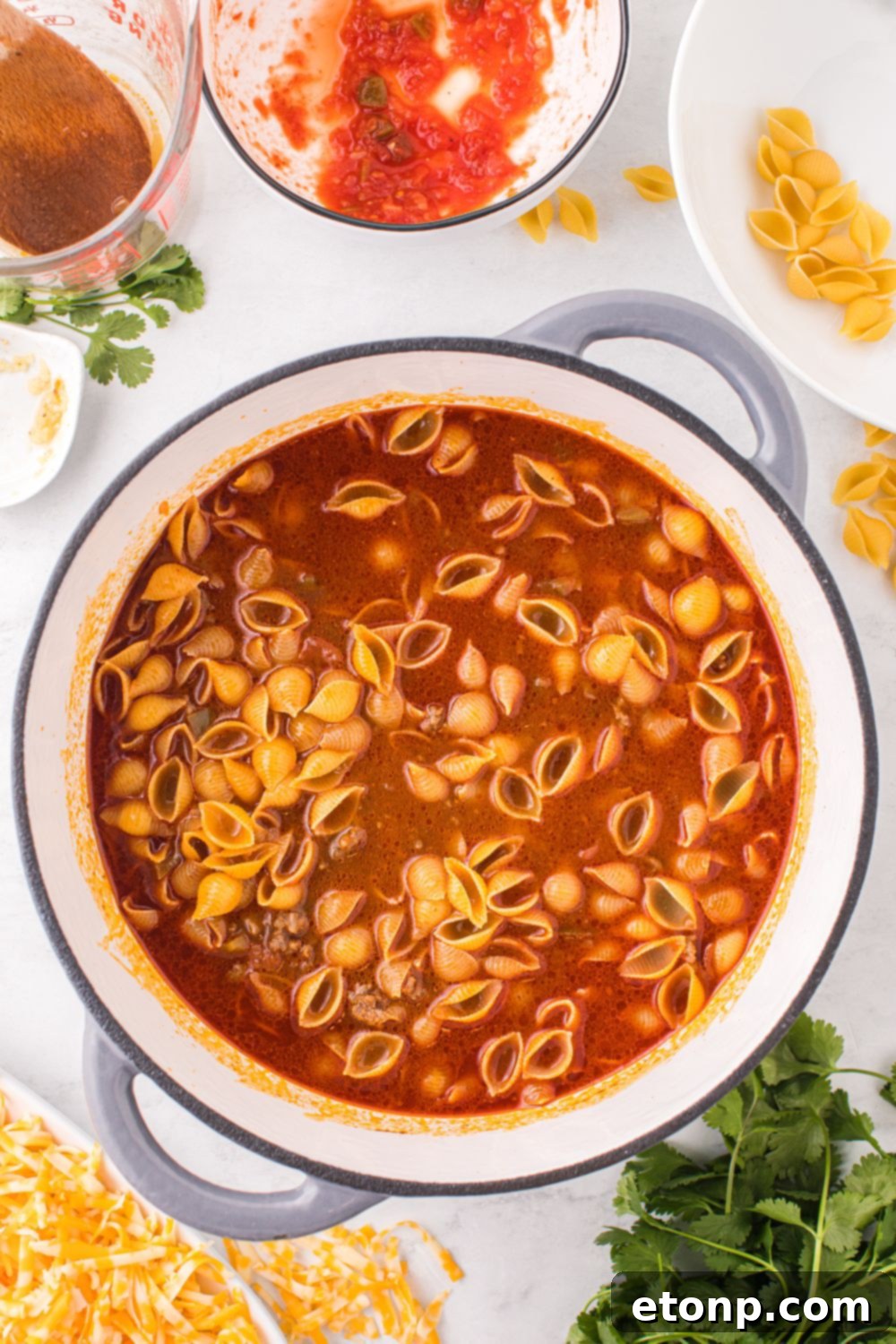 Cheesy Taco Pasta 12 Uncooked pasta shells added to the simmering taco pasta mixture in a pot.