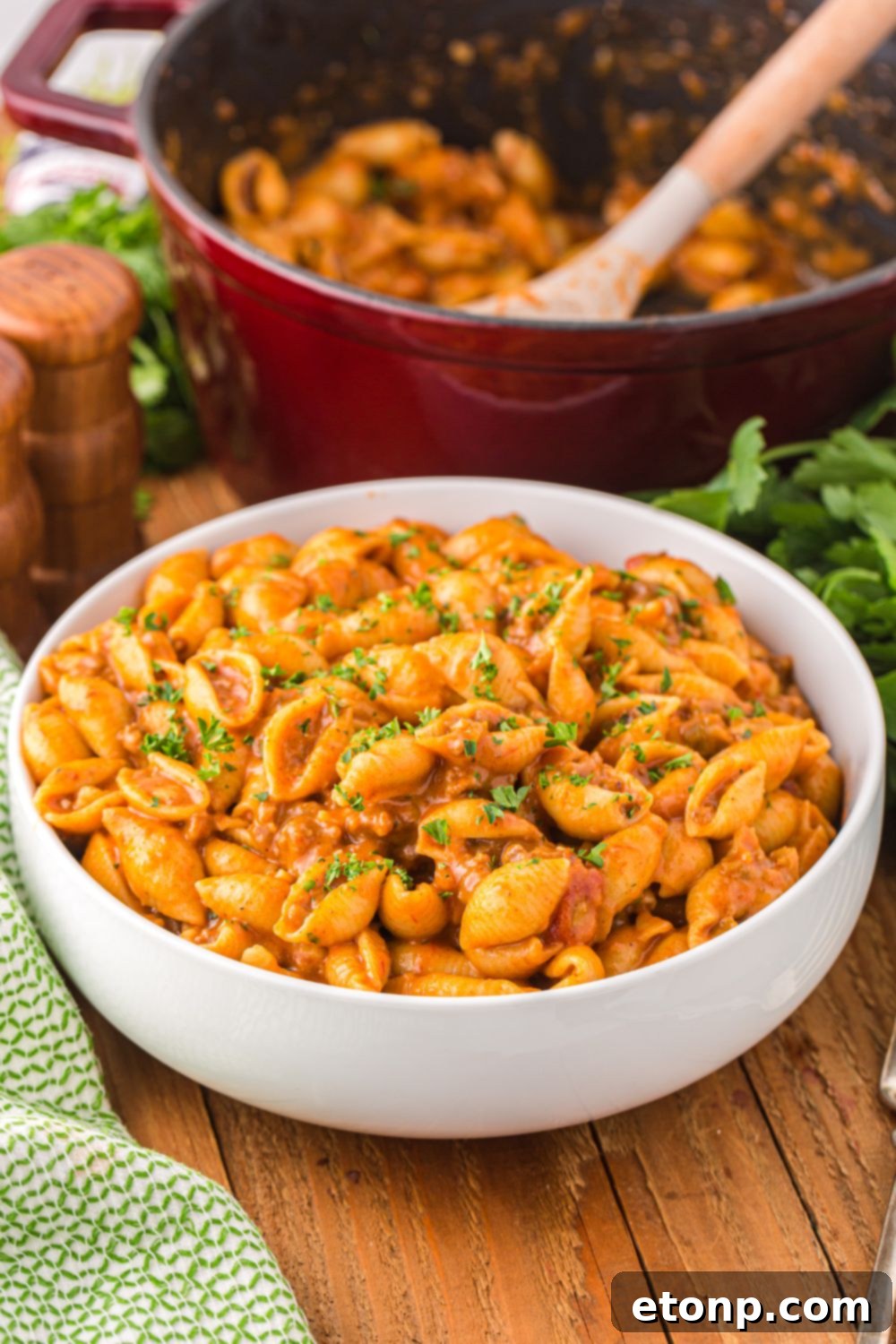 Cheesy Taco Pasta 18 A bowl of taco pasta on a wooden table, with a larger skillet of pasta blurred in the background.