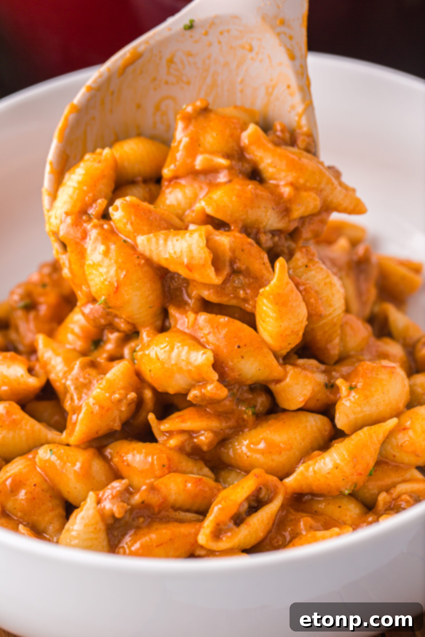 Cheesy Taco Pasta 4 A large white spoon scooping a generous portion of cheesy ground beef taco pasta into a white serving bowl.