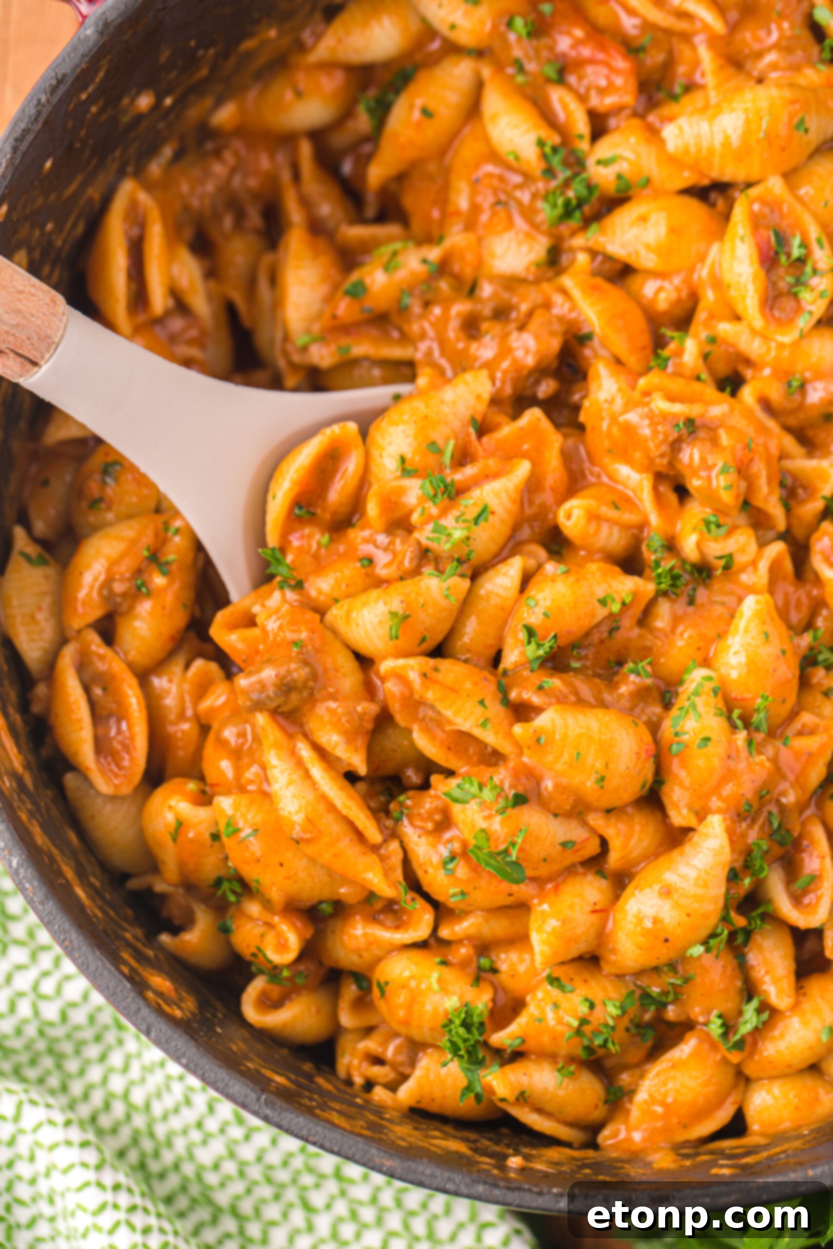 Cheesy Taco Pasta 5 Close-up of taco pasta in a large skillet, with a white spoon showing the creamy, cheesy sauce clinging to the pasta shells.