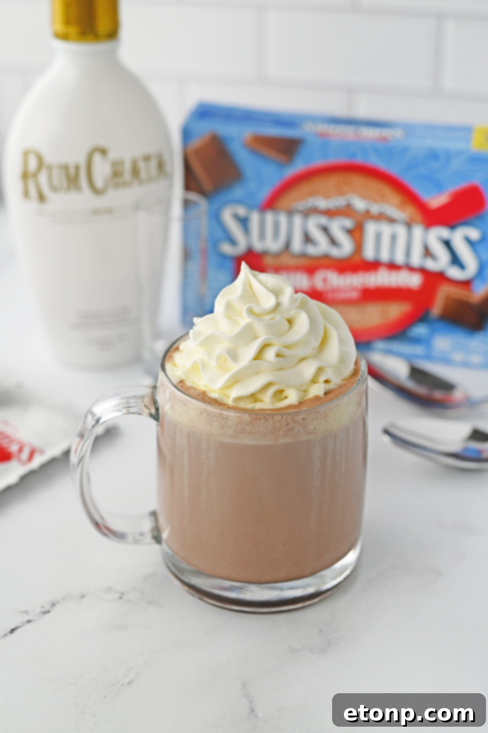 rumchata Hot Chocolate in a clear glass mug topped with whipped cream on a white marble table 