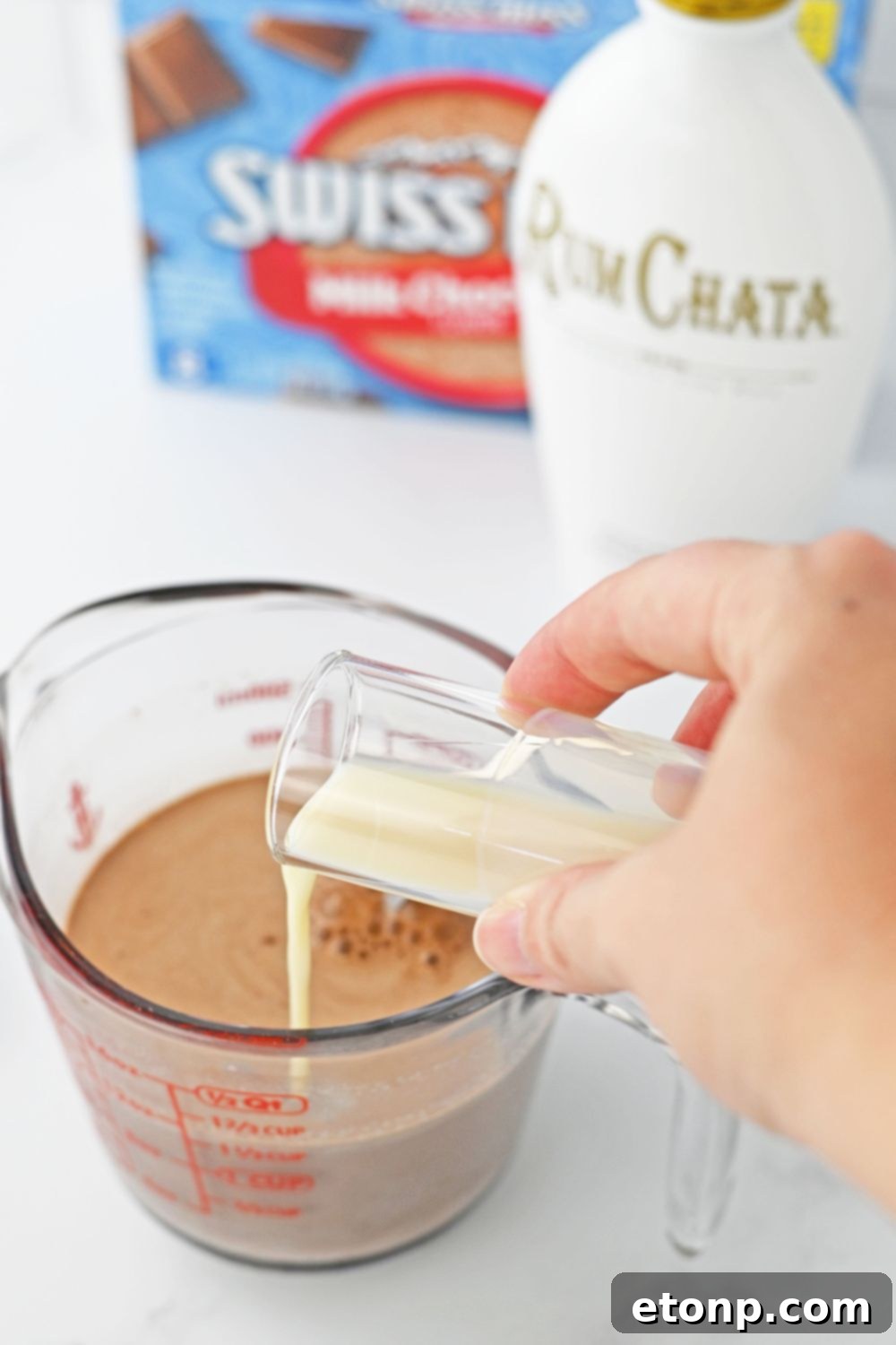 pouring rumchata into a measuring cup with hot chocolate 