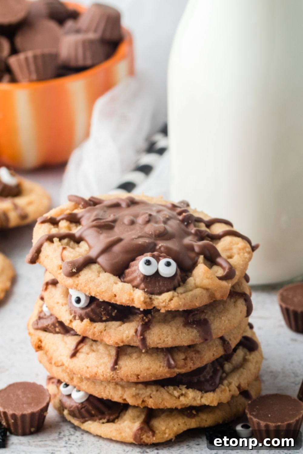 Frightfully Delicious Peanut Butter Spider Cookies 6 stacked cookies that look like spiders on table with milk behind it in a glass jar