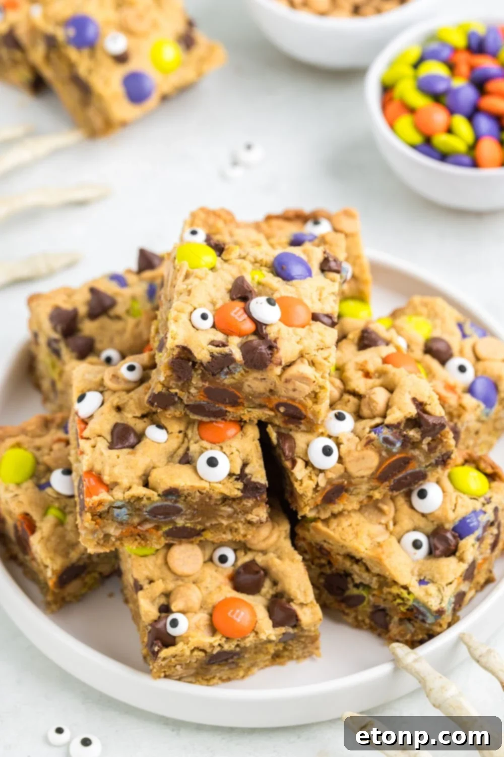 a stack of many halloween monster cookie bars on a white plate
