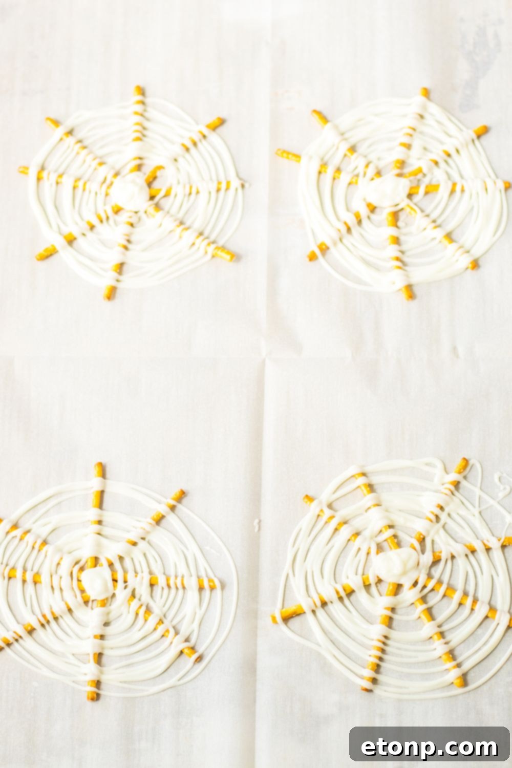 White chocolate being swirled in circles on top of the pretzels to mimic a spider web